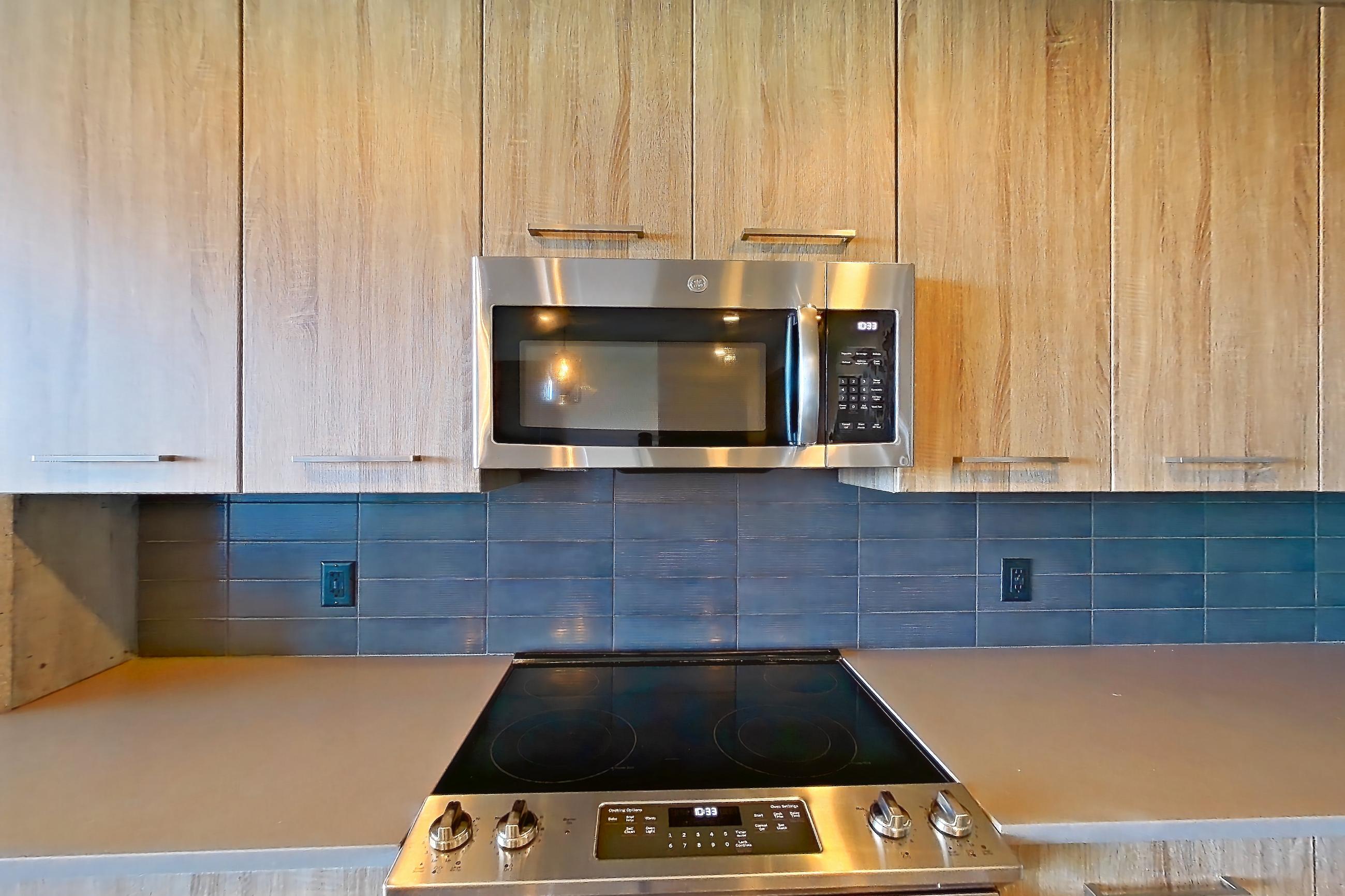 Kitchen with dark countertops, dishwasher, electric range, light countertops, light stone countertops, light wood-finish flooring, microwave, oven/range, refrigerator, stainless steel appliances, and water & ice dispenser, Apartment 1108 at Cortland Glenwood South