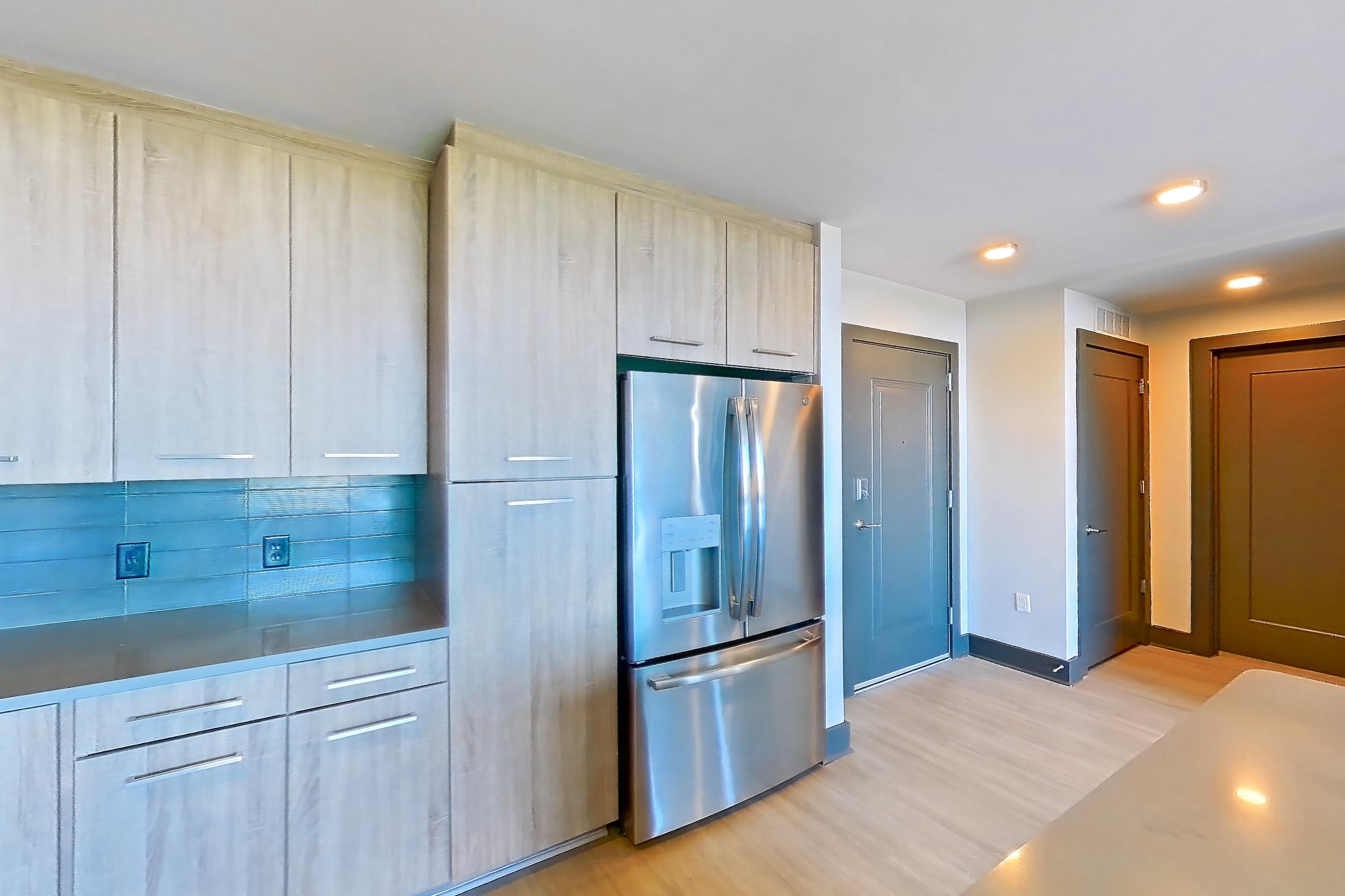 Kitchen with dark countertops, dishwasher, electric range, light countertops, light stone countertops, light wood-finish flooring, microwave, oven/range, refrigerator, stainless steel appliances, and water & ice dispenser, Apartment 1108 at Cortland Glenwood South