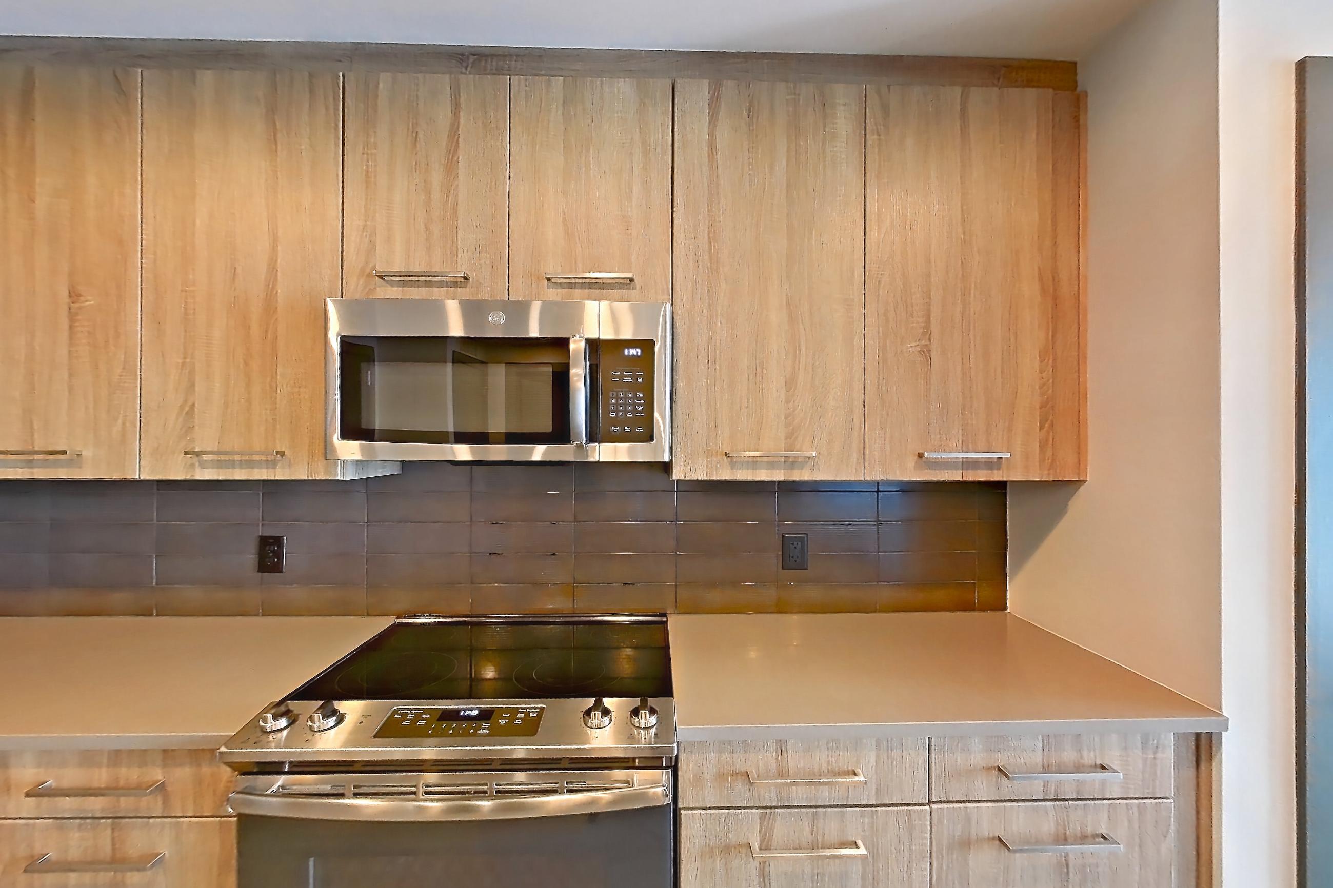 Kitchen with electric range, light countertops, light wood-finish flooring, microwave, oven/range, refrigerator, stainless steel appliances, and water & ice dispenser, Apartment 1113 at Cortland Glenwood South