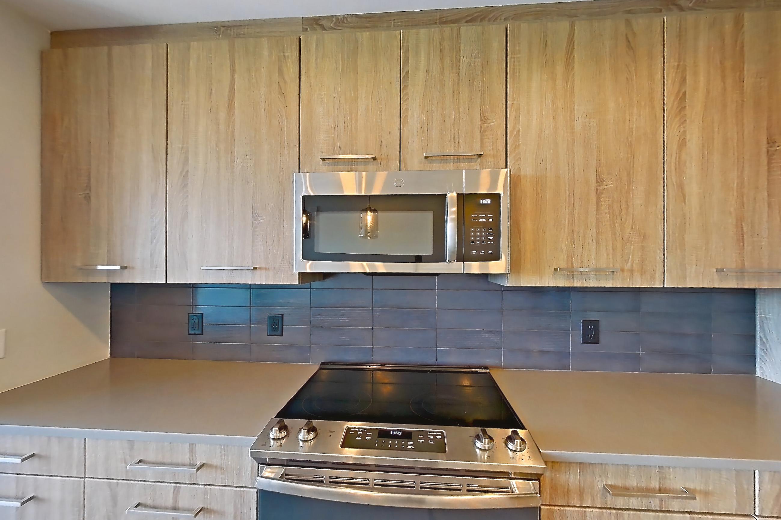 Kitchen with dark countertops, electric range, light countertops, light wood-finish flooring, microwave, oven/range, refrigerator, stainless steel appliances, and water & ice dispenser, Apartment 1116 at Cortland Glenwood South