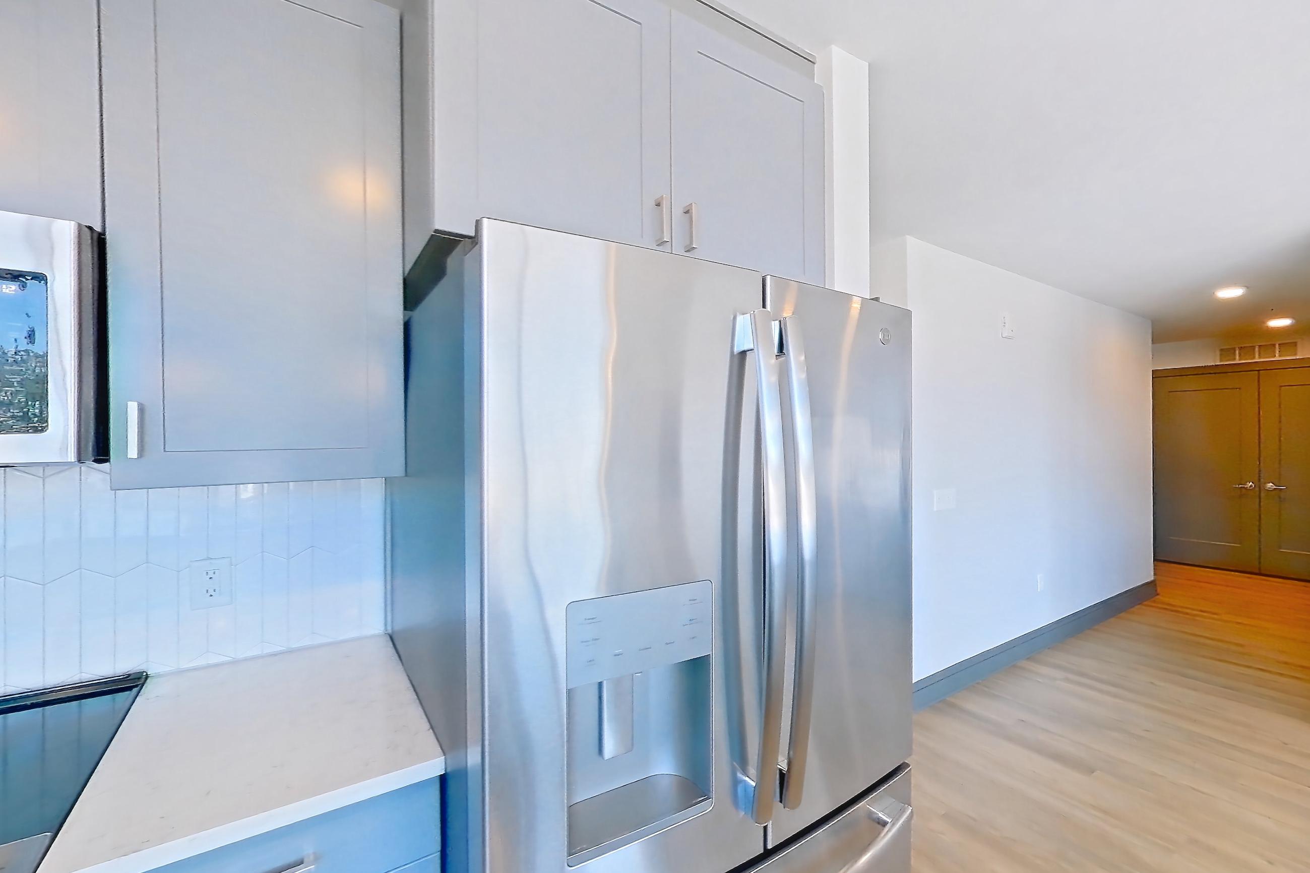 Kitchen with dishwasher, electric range, kitchen island, light countertops, light stone countertops, light wood-finish flooring, oven/range, refrigerator, stainless steel appliances, and water & ice dispenser, Apartment 430 at Cortland Glenwood South