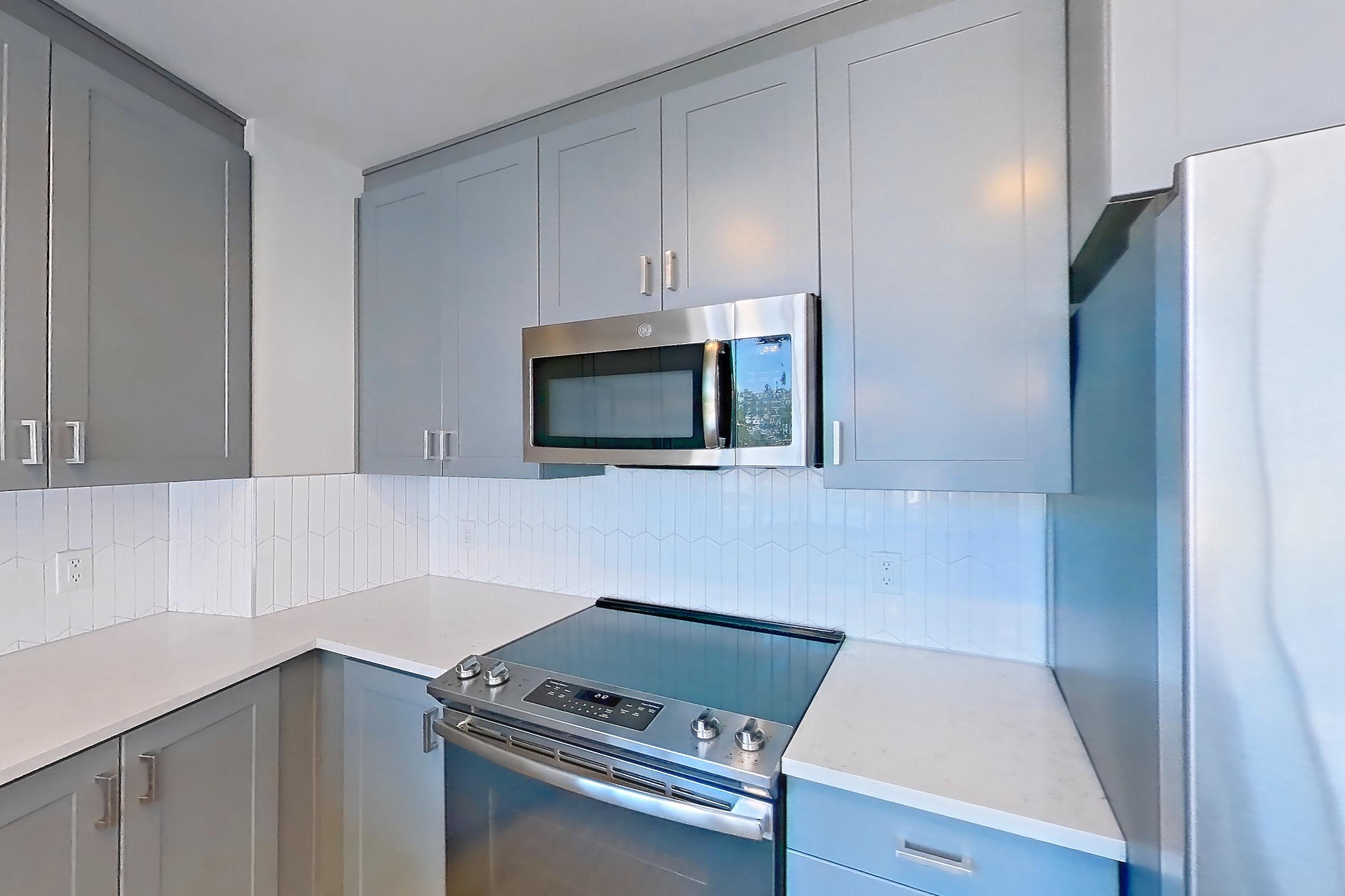 Kitchen with dishwasher, electric range, kitchen island, light countertops, light stone countertops, light wood-finish flooring, oven/range, refrigerator, stainless steel appliances, and water & ice dispenser, Apartment 430 at Cortland Glenwood South