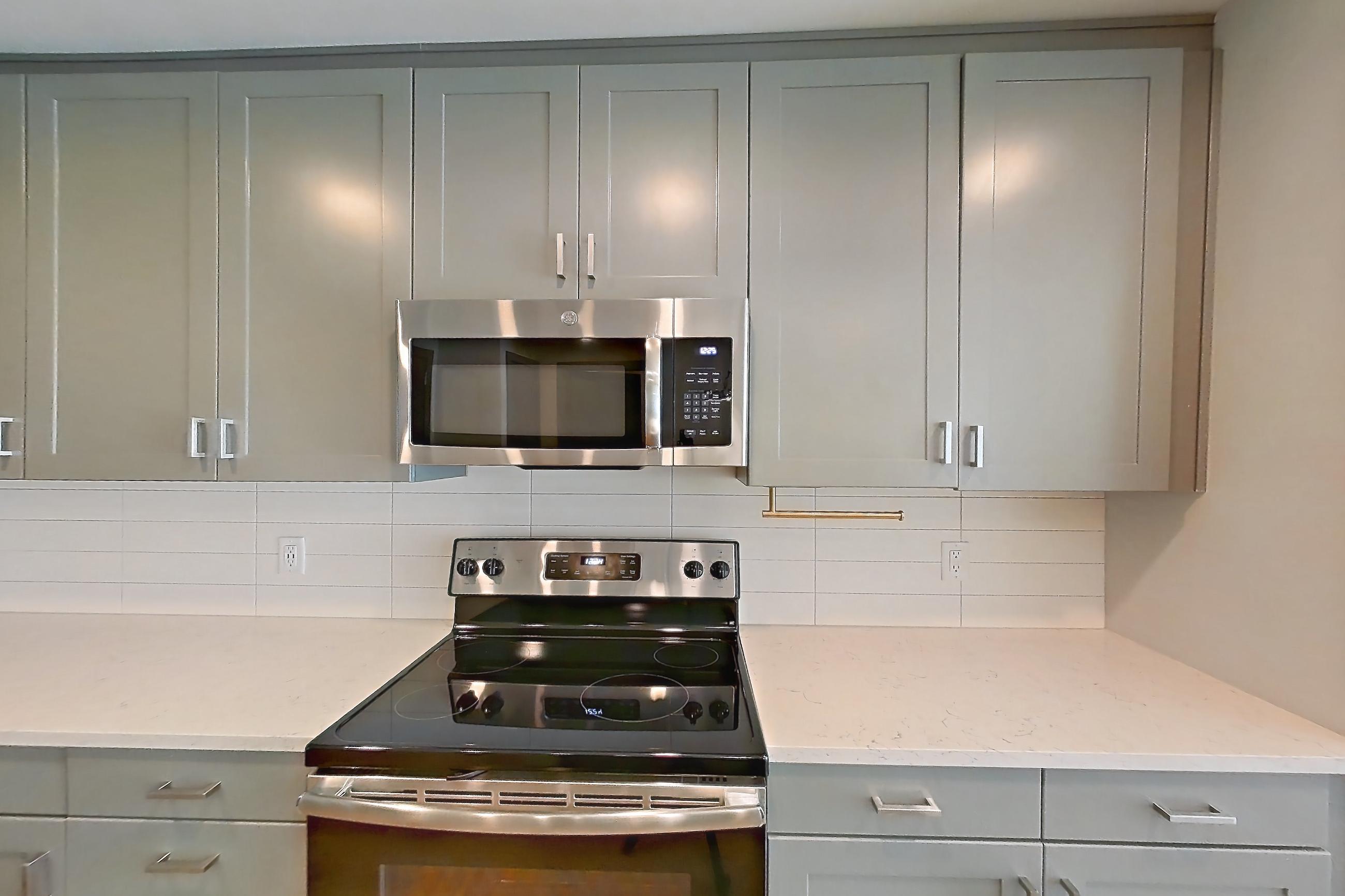 Kitchen with electric range, light countertops, light stone countertops, light wood-finish flooring, microwave, oven/range, refrigerator, stainless steel appliances, and water & ice dispenser, Apartment 813 at Cortland Glenwood South