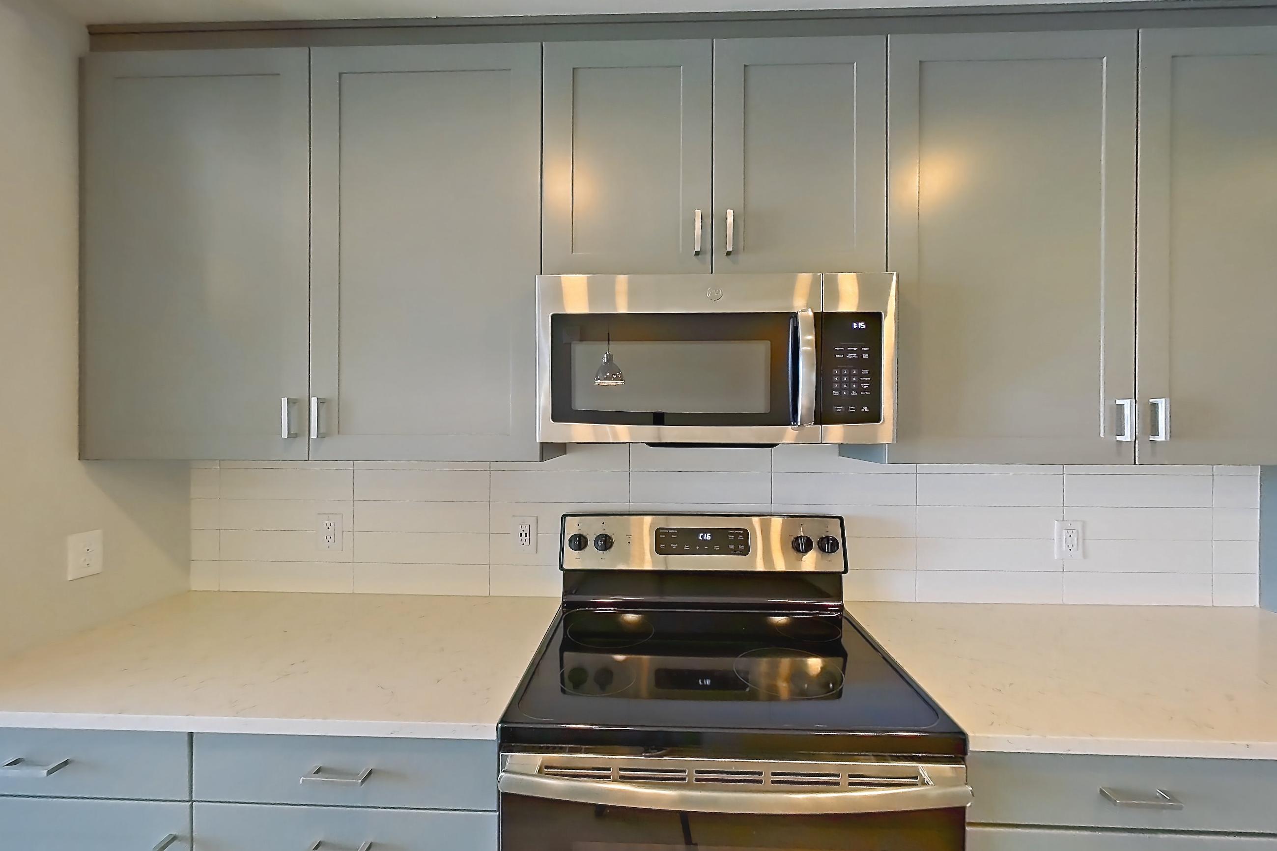 Kitchen with electric range, light countertops, light stone countertops, light wood-finish flooring, microwave, oven/range, refrigerator, stainless steel appliances, and water & ice dispenser, Apartment 816 at Cortland Glenwood South
