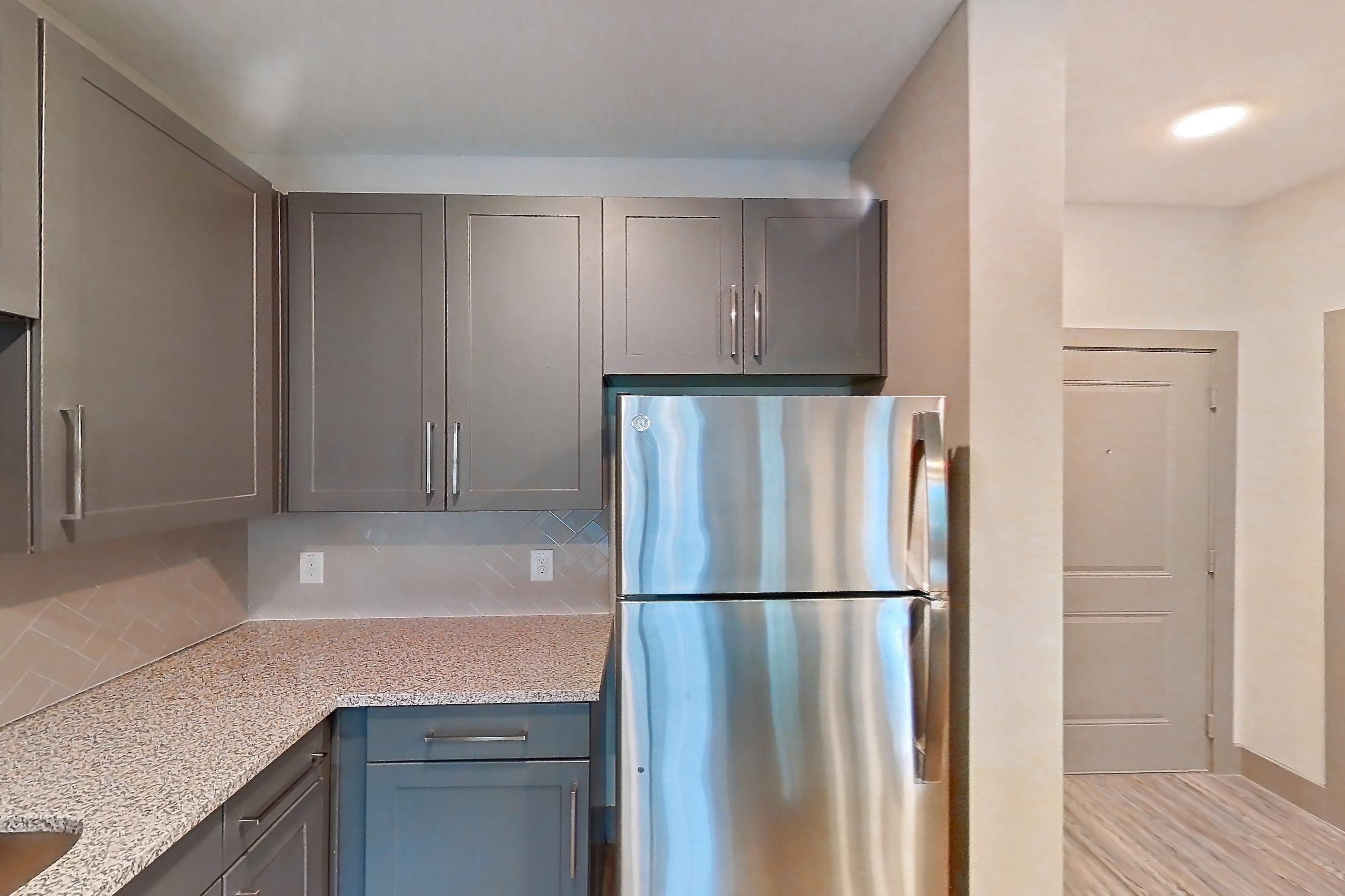 Kitchen with dishwasher, electric range, light countertops, light stone countertops, light wood-finish flooring, microwave, oven/range, refrigerator, and stainless steel appliances, Apartment 05104 at Embree Hill
