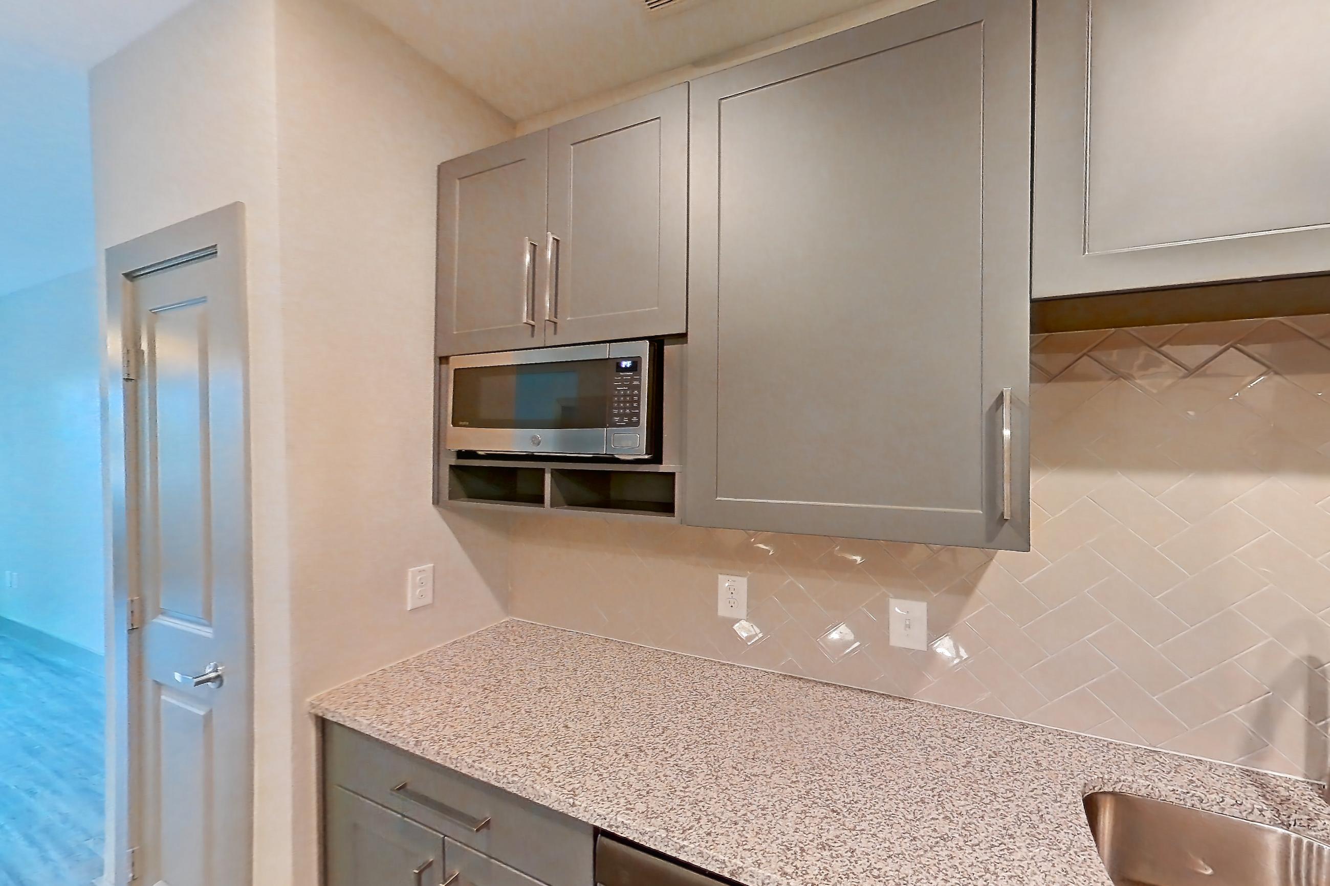 Kitchen with dishwasher, electric range, light countertops, light stone countertops, light wood-finish flooring, microwave, oven/range, refrigerator, and stainless steel appliances, Apartment 05104 at Embree Hill