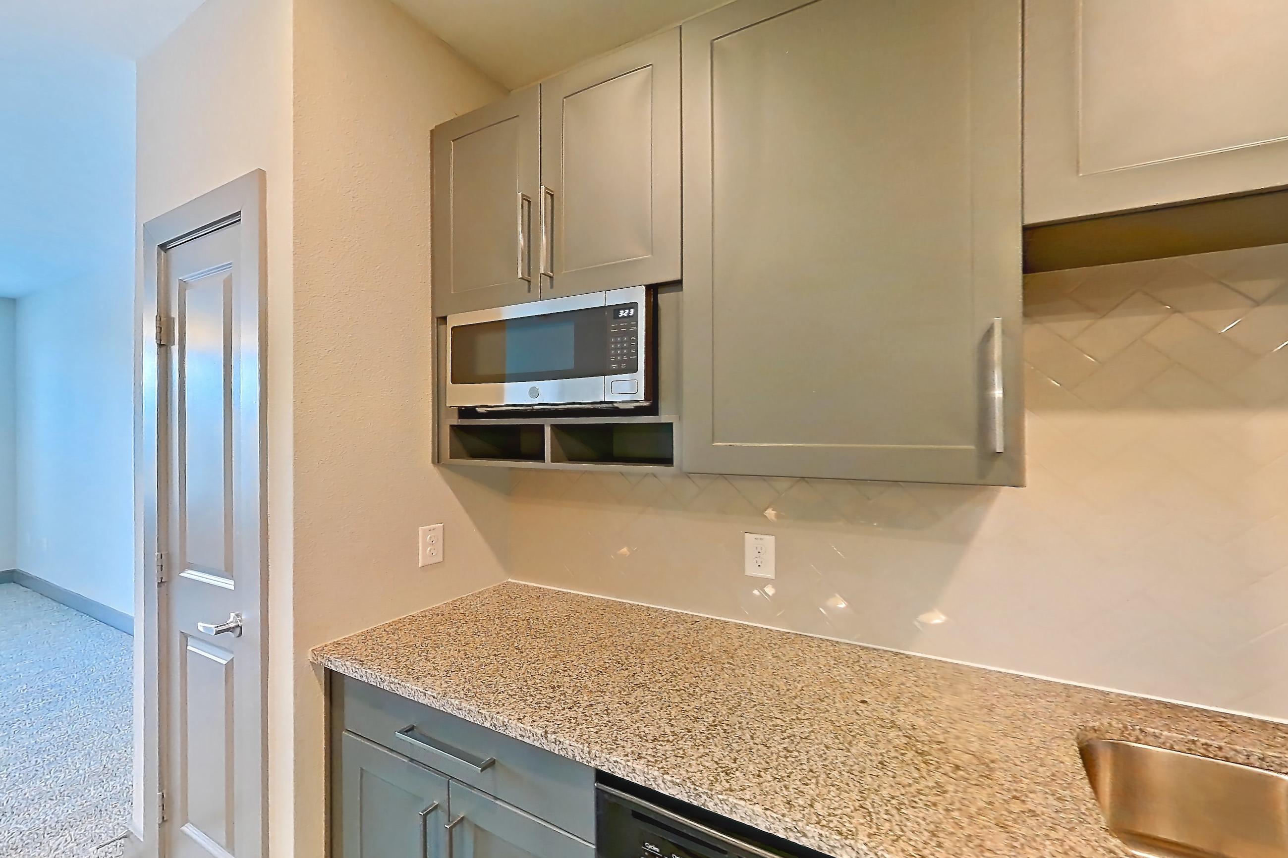 Kitchen with dishwasher, electric range, light countertops, light stone countertops, light wood-finish flooring, microwave, oven/range, refrigerator, and stainless steel appliances, Apartment 05205 at Embree Hill