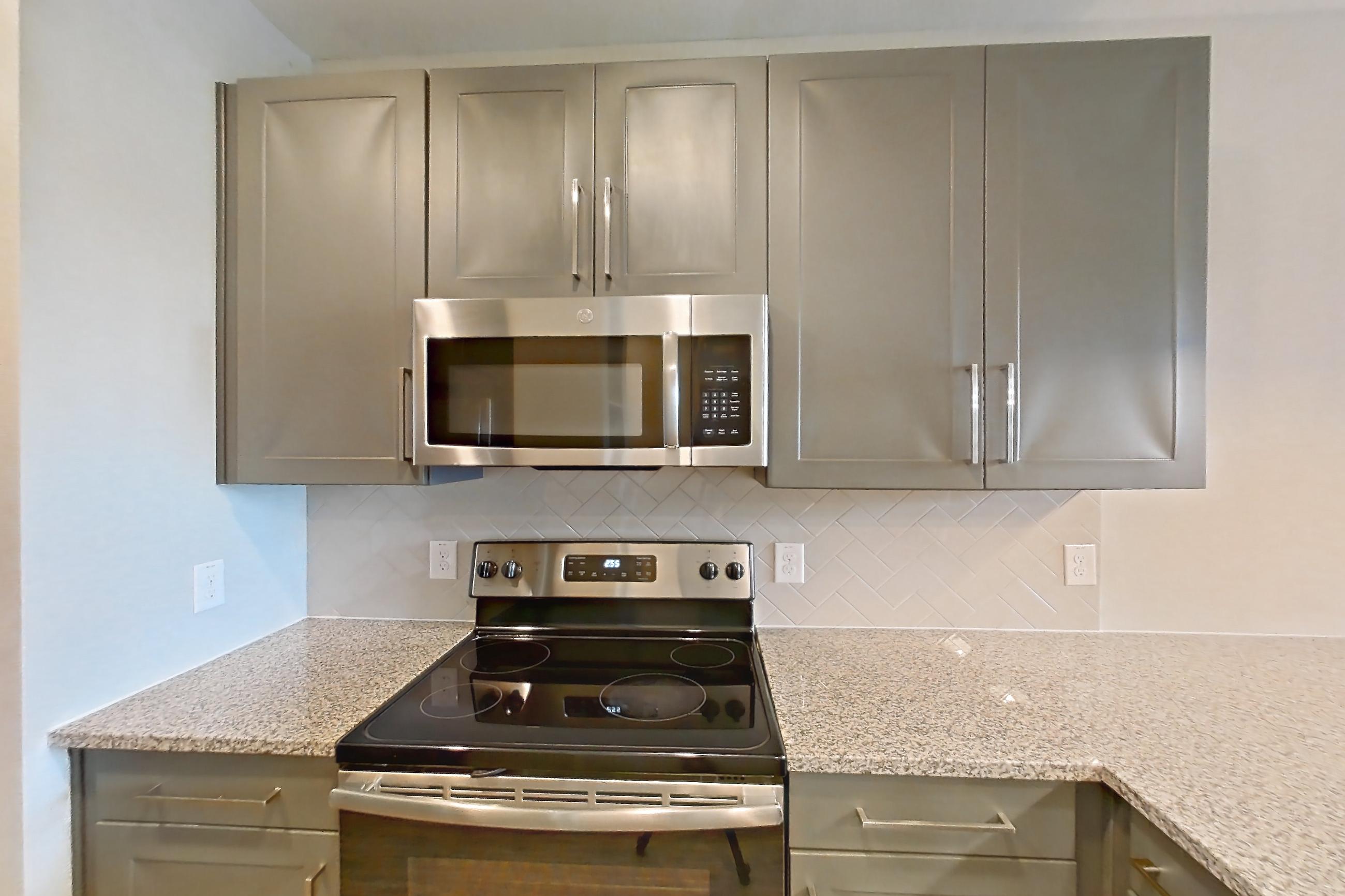 Kitchen with dishwasher, electric range, light countertops, light stone countertops, light wood-finish flooring, microwave, oven/range, refrigerator, and stainless steel appliances, Apartment 05103 at Embree Hill