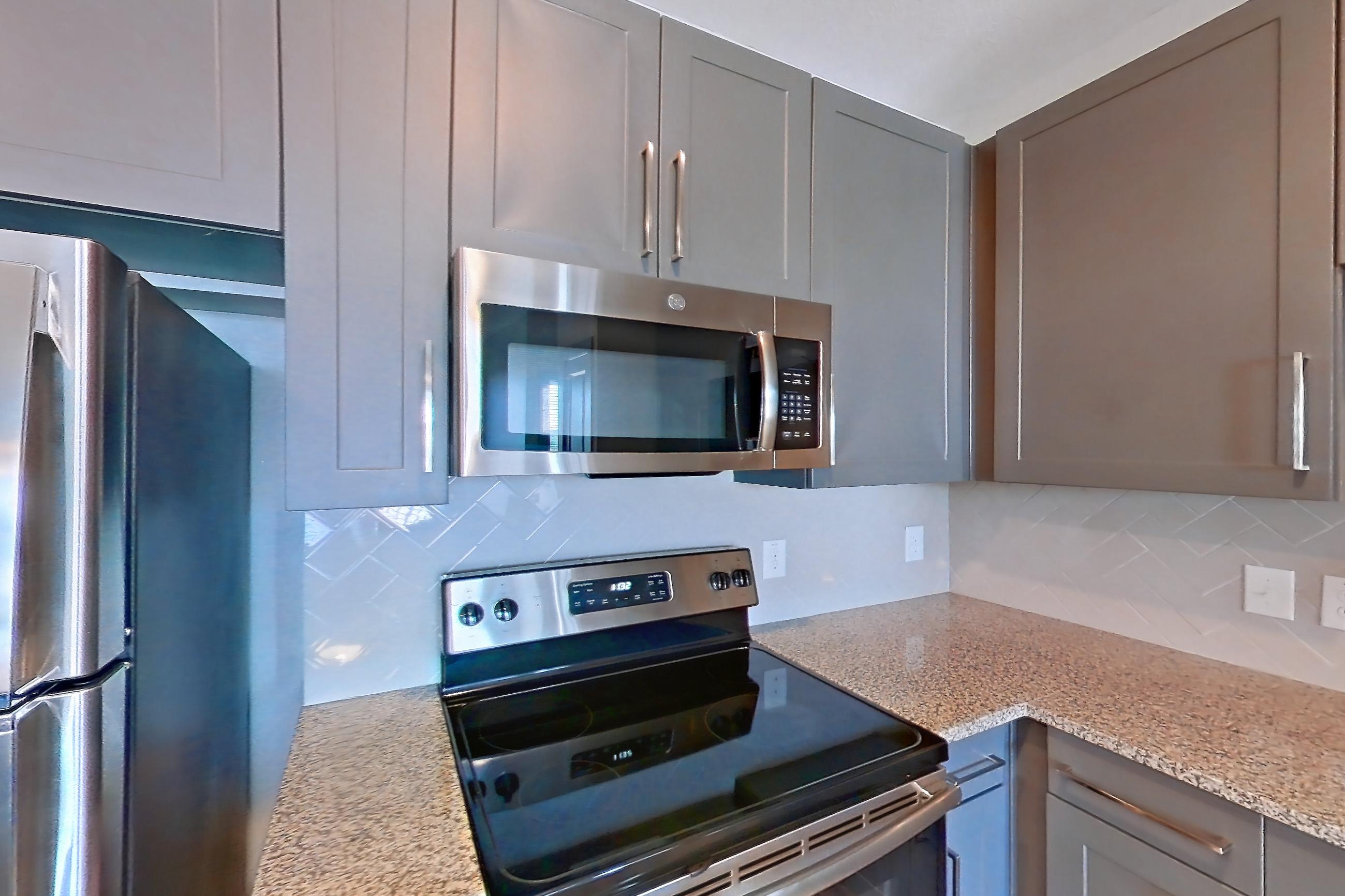 Kitchen with dishwasher, electric range, light carpet, light stone countertops, light wood-finish flooring, microwave, oven/range, refrigerator, and stainless steel appliances, Apartment 05302 at Embree Hill