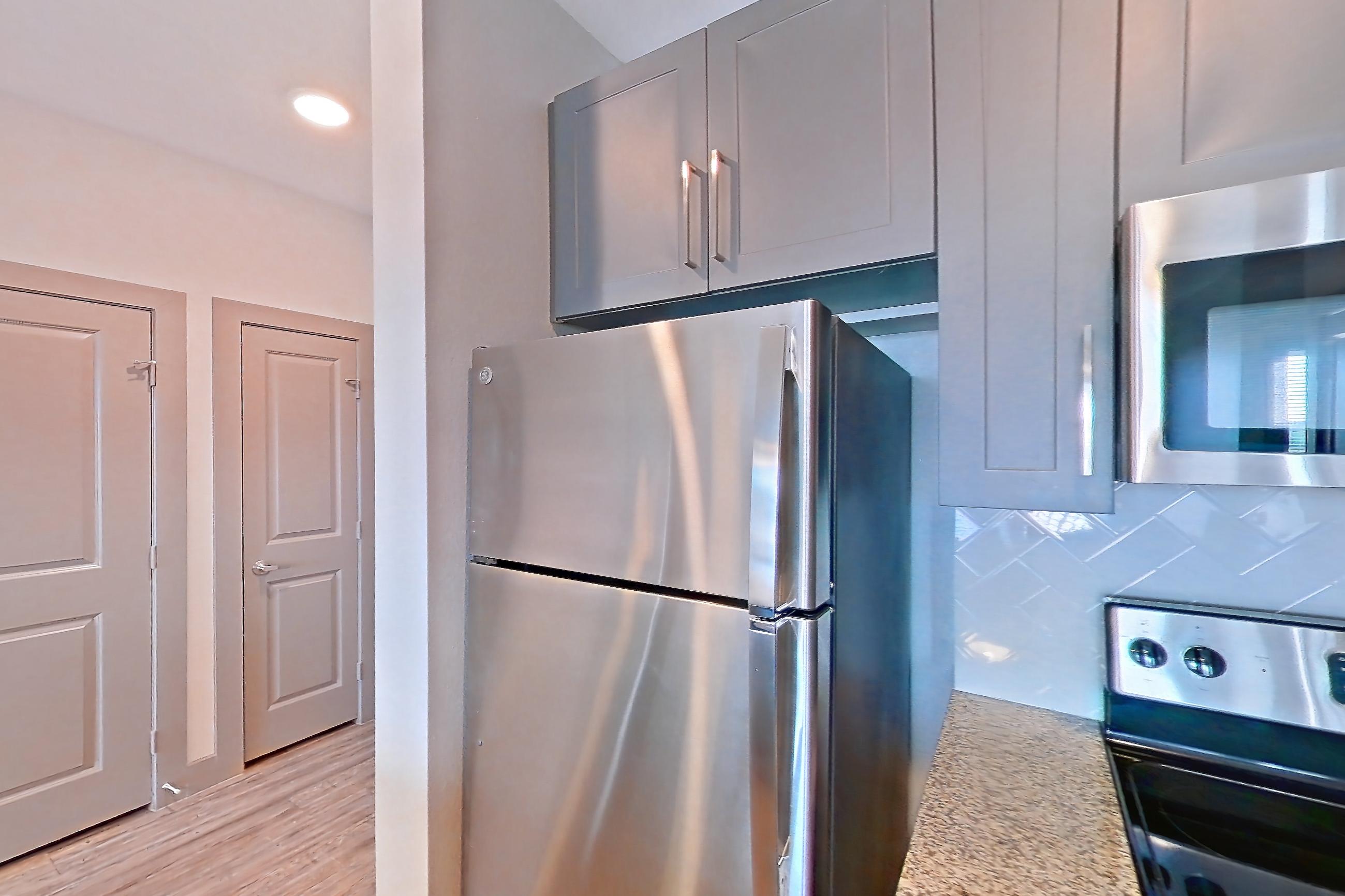 Kitchen with dishwasher, electric range, light carpet, light stone countertops, light wood-finish flooring, microwave, oven/range, refrigerator, and stainless steel appliances, Apartment 05302 at Embree Hill