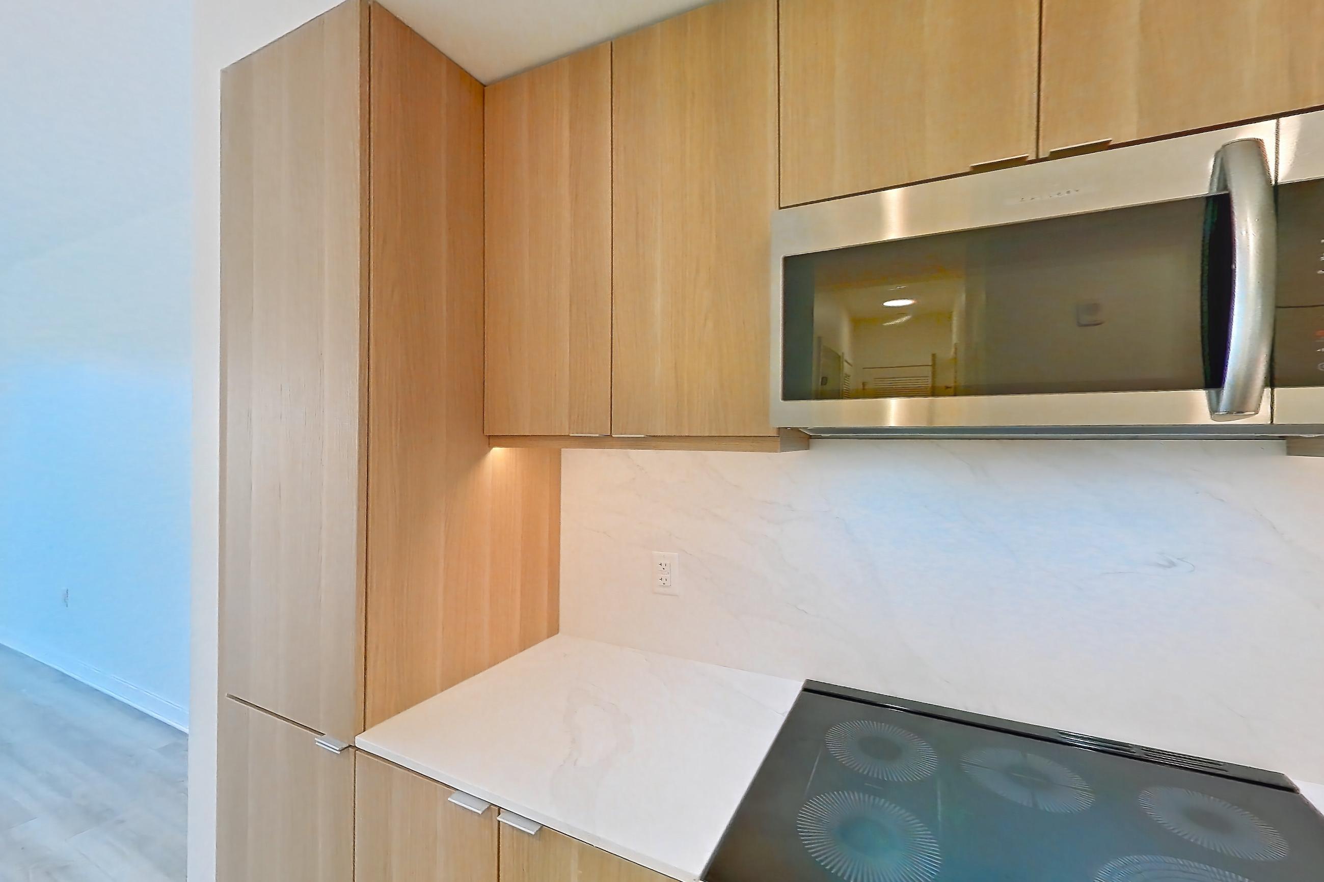 Kitchen with electric range, kitchen island, light countertops, light stone countertops, light wood-finish flooring, microwave, oven/range, and stainless steel appliances, Apartment 416 at Residences at Mazza