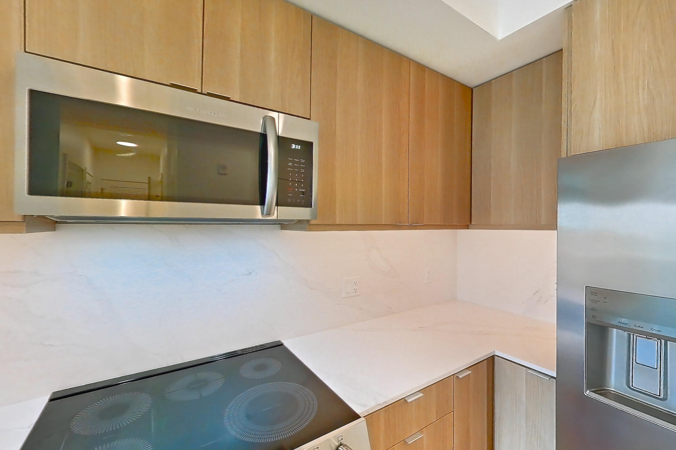 Kitchen with electric range, kitchen island, light countertops, light stone countertops, light wood-finish flooring, microwave, oven/range, and stainless steel appliances, Apartment 416 at Residences at Mazza