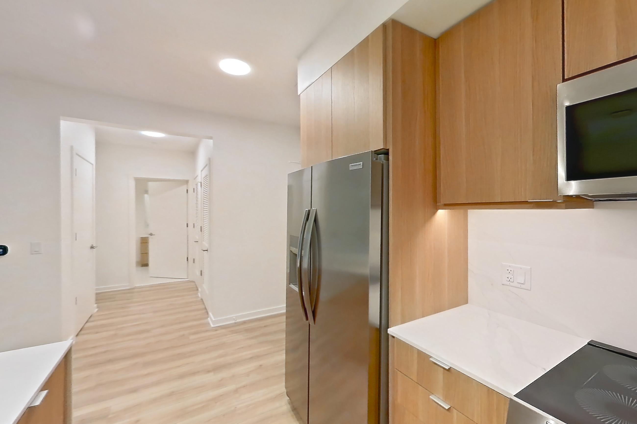 Kitchen with electric range, light countertops, light stone countertops, light wood-finish flooring, microwave, oven/range, refrigerator, stainless steel appliances, and water & ice dispenser, Apartment 305 at Residences at Mazza