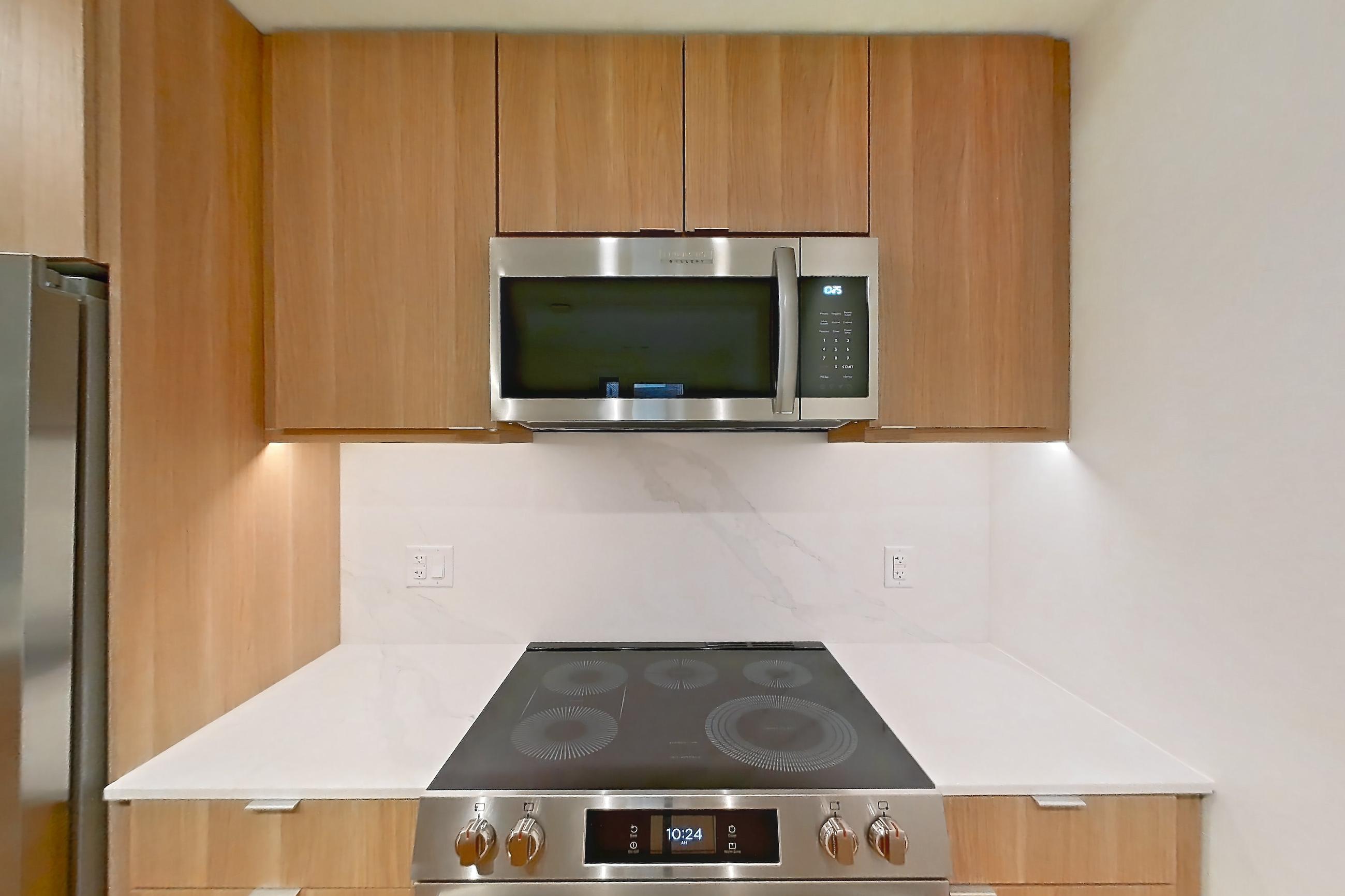 Kitchen with electric range, light countertops, light stone countertops, light wood-finish flooring, microwave, oven/range, refrigerator, stainless steel appliances, and water & ice dispenser, Apartment 305 at Residences at Mazza