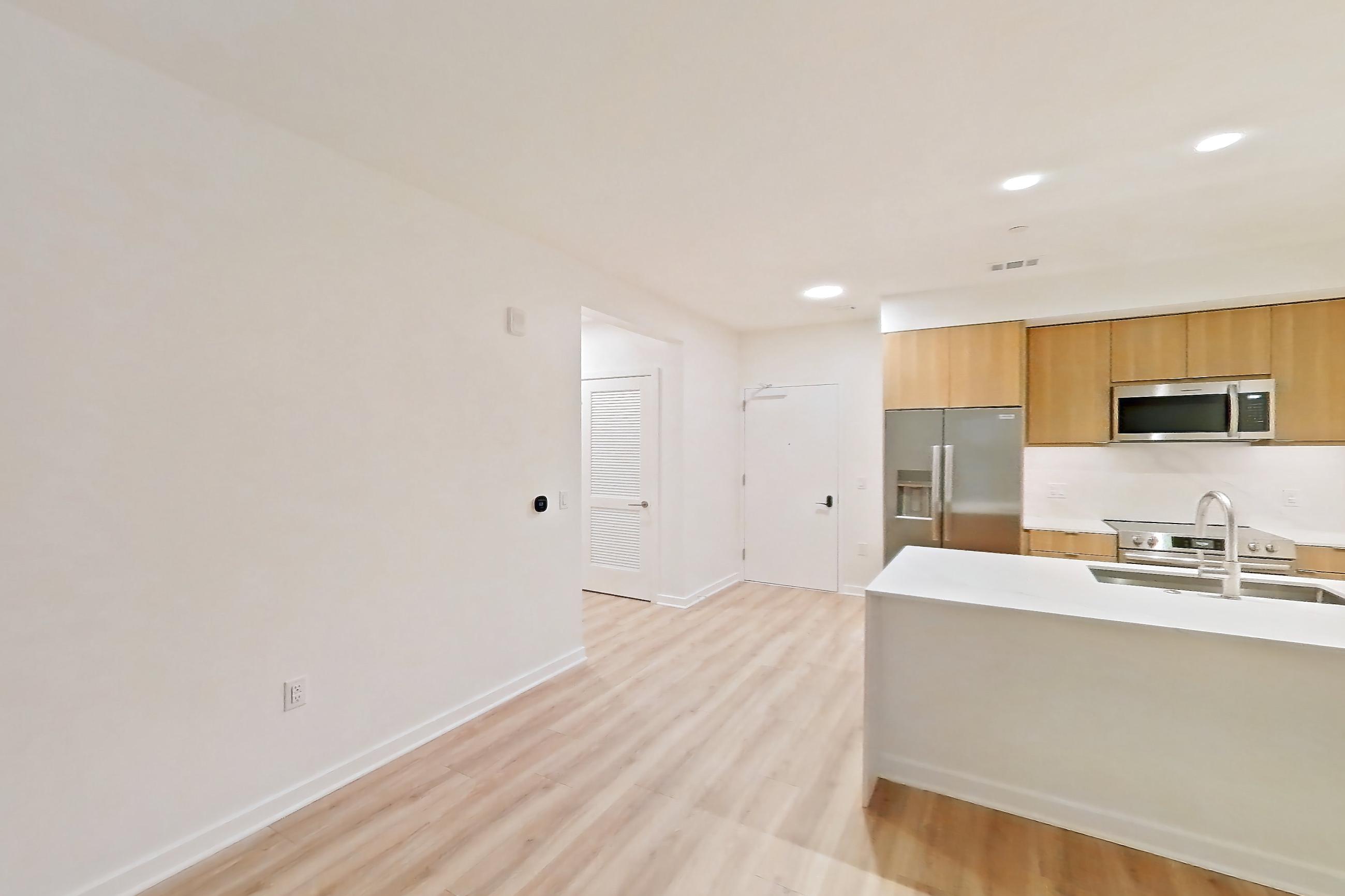 Living room with light countertops, light wood-finish flooring, microwave, oven/range, refrigerator, stainless steel appliances, and water & ice dispenser, Apartment 305 at Residences at Mazza