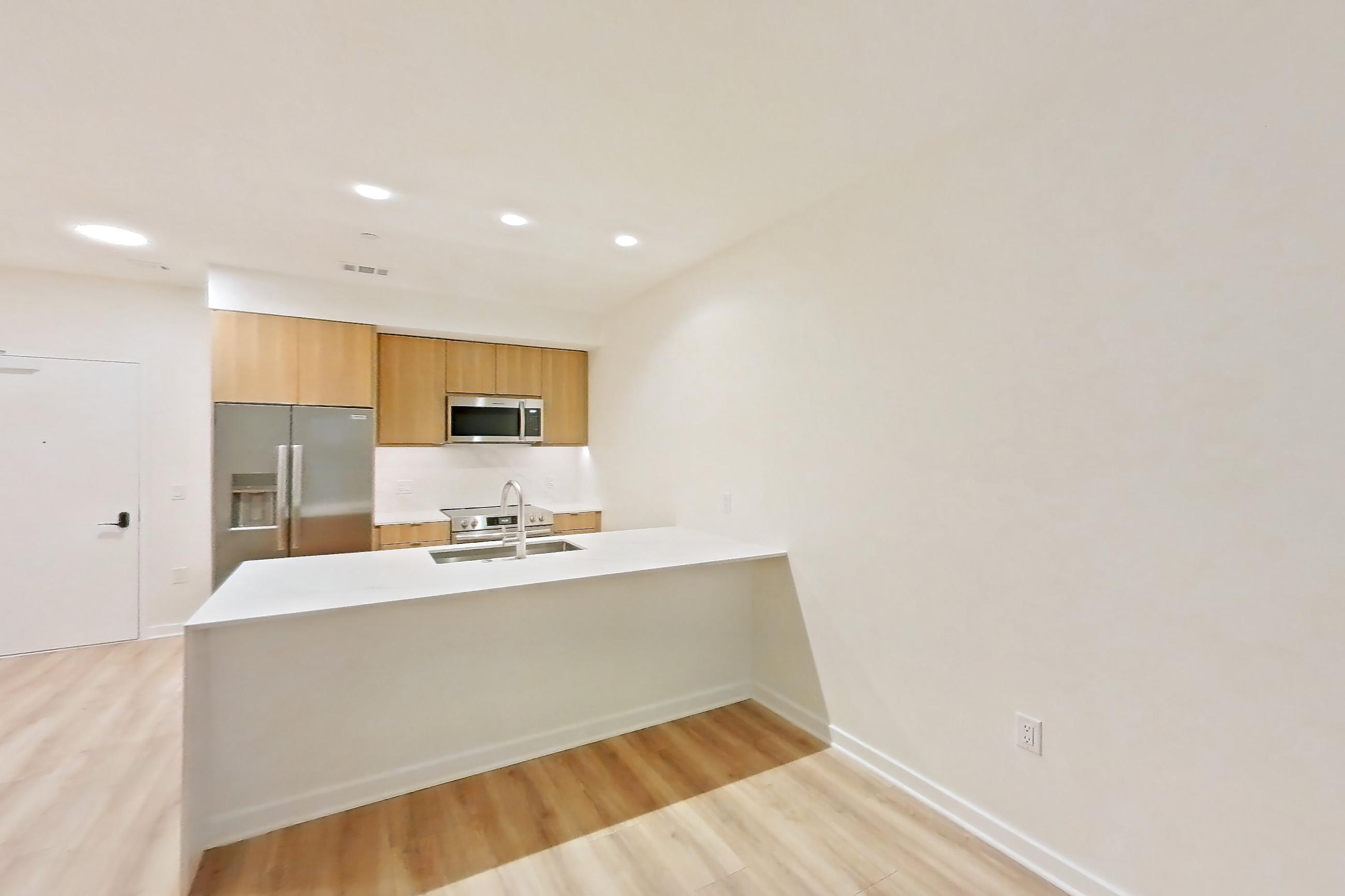 Living room with light countertops, light wood-finish flooring, microwave, oven/range, refrigerator, stainless steel appliances, and water & ice dispenser, Apartment 305 at Residences at Mazza