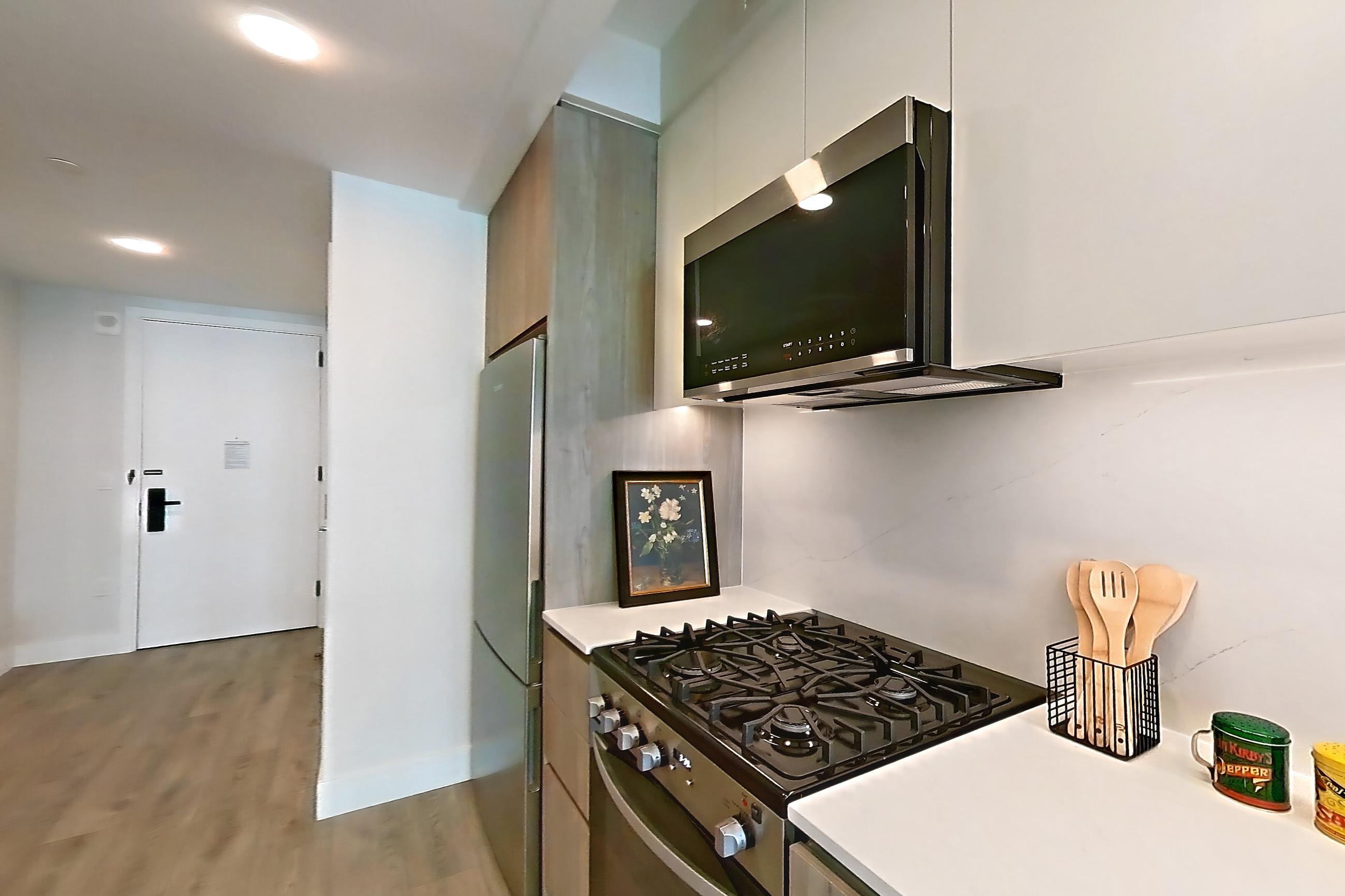 Kitchen with gas range, light stone countertops, light wood-finish flooring, microwave, oven/range, refrigerator, and stainless steel appliances, Apartment 1339 at Loden