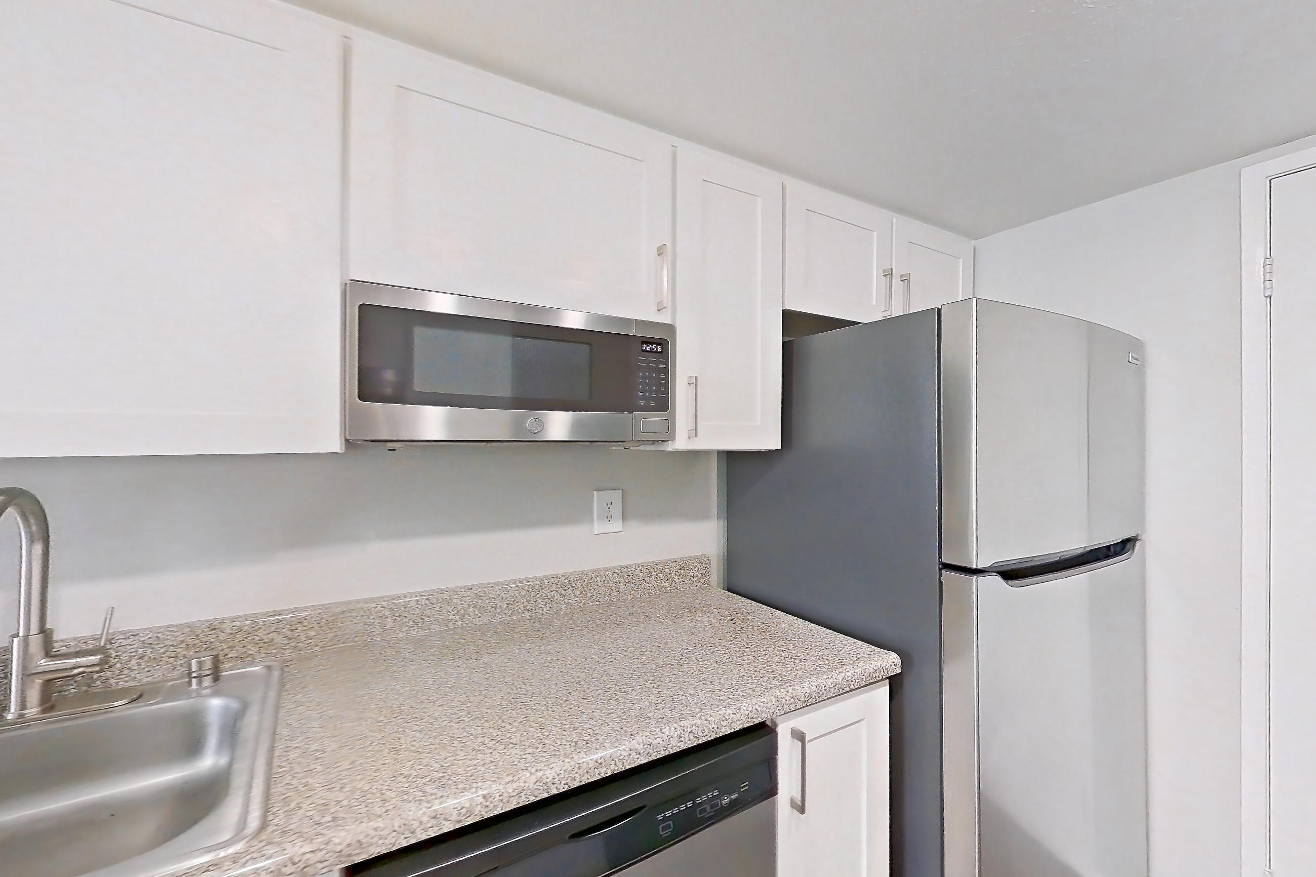 Kitchen with dishwasher, electric range, light countertops, light stone countertops, light wood-finish flooring, microwave, oven/range, range hood, refrigerator, and stainless steel appliances, Apartment 09 at Avana Rancho Cucamonga