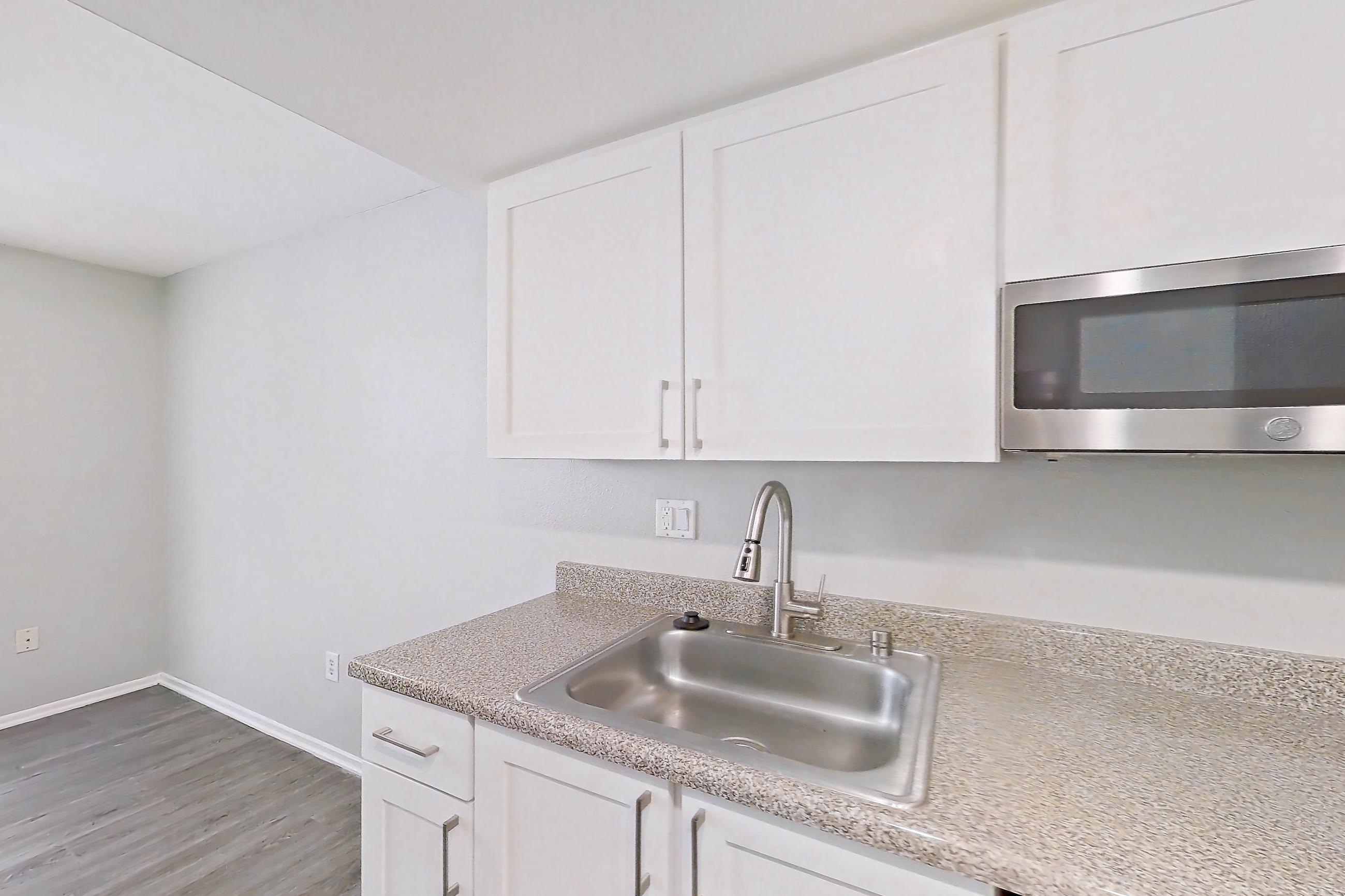 Kitchen with dishwasher, electric range, light countertops, light stone countertops, light wood-finish flooring, microwave, oven/range, range hood, refrigerator, and stainless steel appliances, Apartment 09 at Avana Rancho Cucamonga