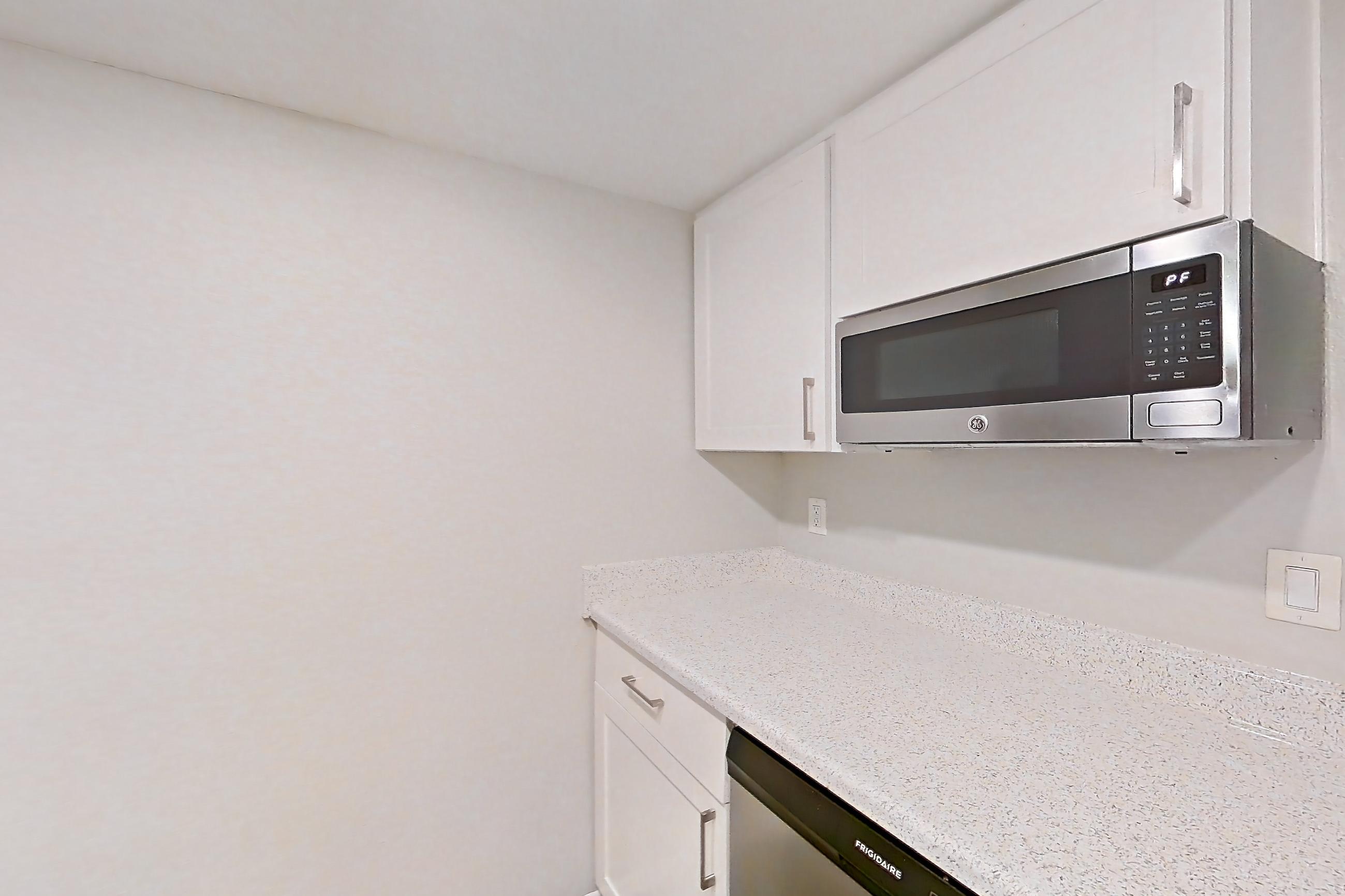 Kitchen with dishwasher, electric range, light countertops, light stone countertops, light wood-finish flooring, oven/range, range hood, refrigerator, and stainless steel appliances, Apartment 12 at Avana Rancho Cucamonga
