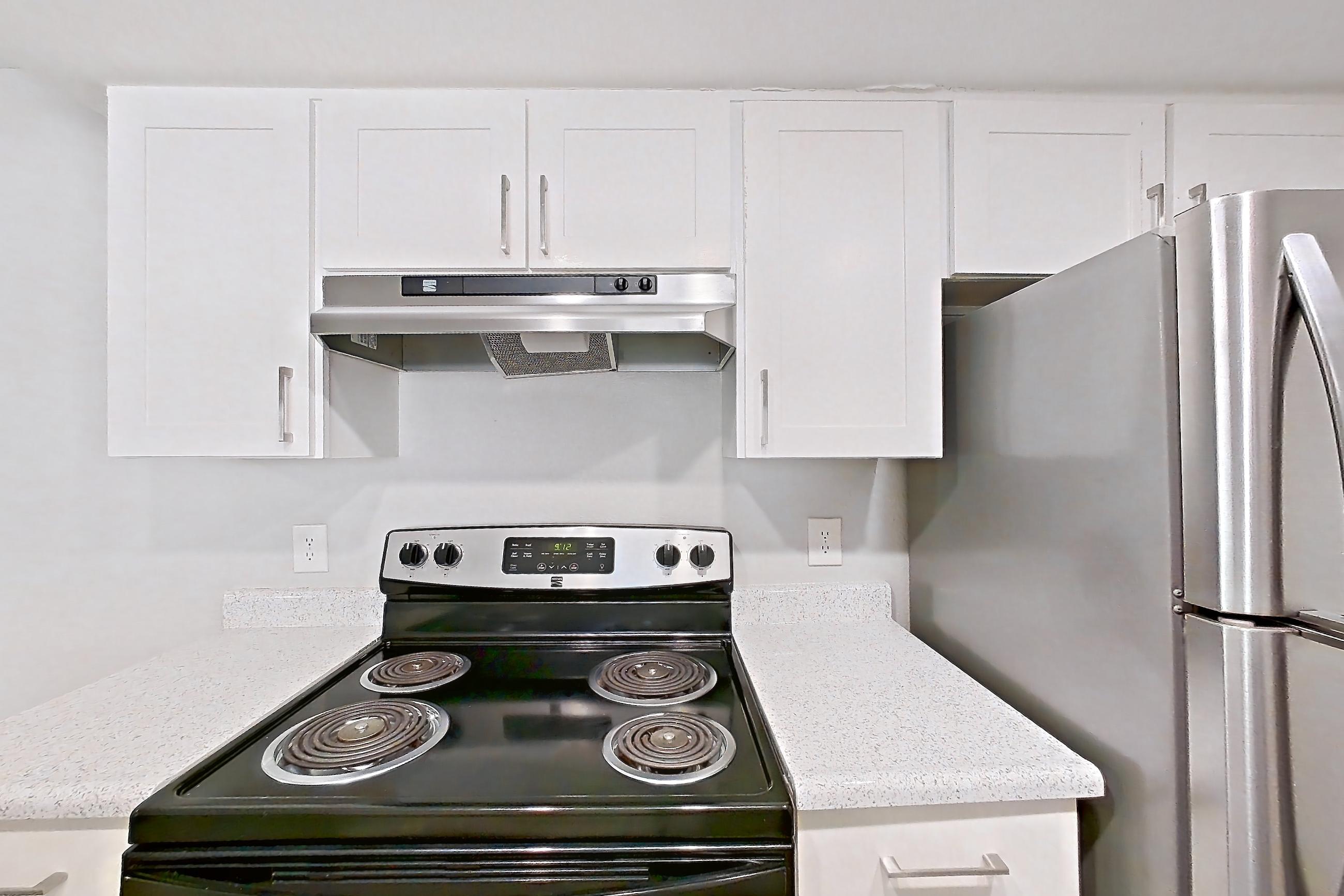 Kitchen with dishwasher, electric range, light countertops, light stone countertops, light wood-finish flooring, oven/range, range hood, refrigerator, and stainless steel appliances, Apartment 12 at Avana Rancho Cucamonga