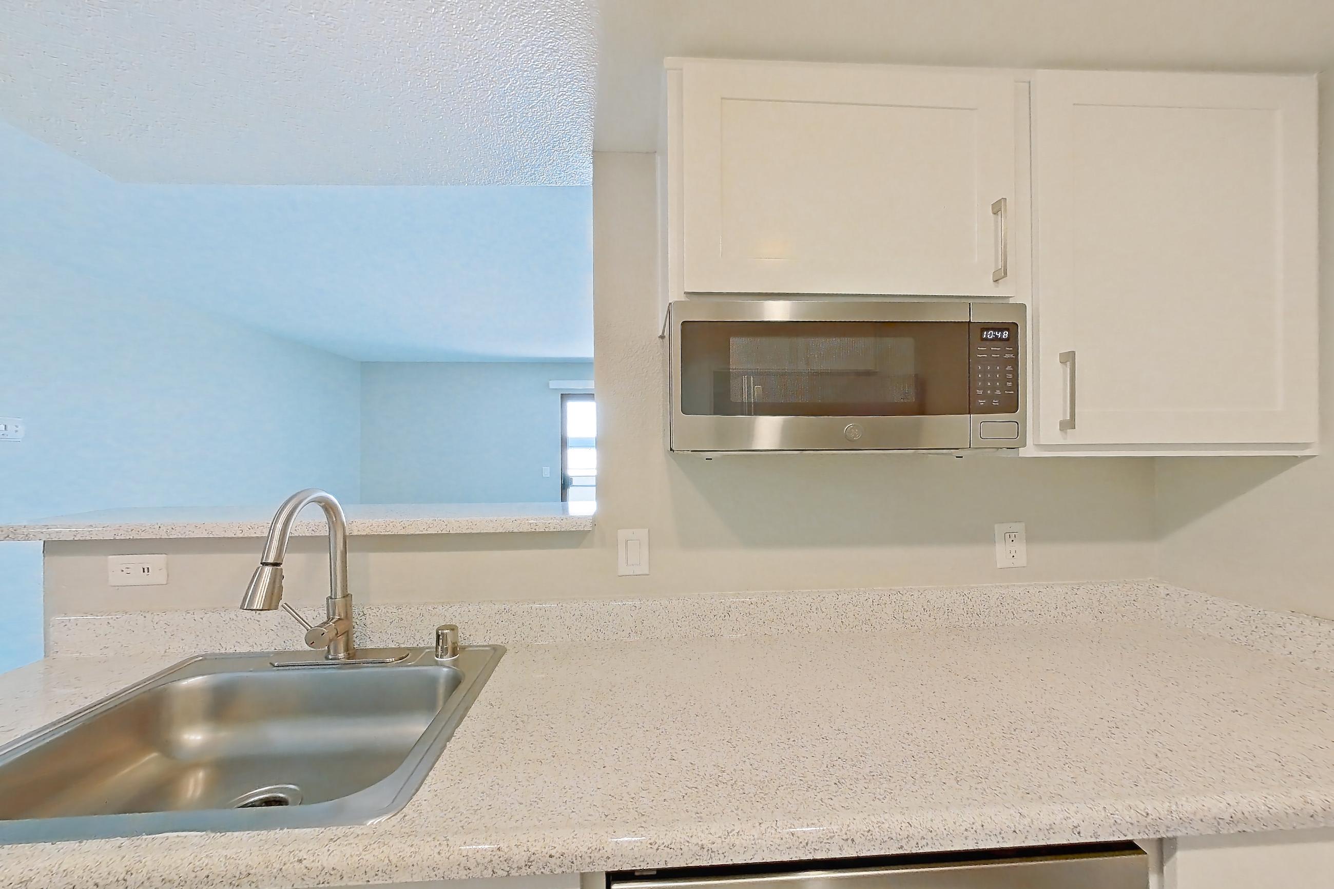 Kitchen with dishwasher, electric range, light stone countertops, light wood-finish flooring, microwave, refrigerator, and stainless steel appliances, Apartment 10 at Avana Rancho Cucamonga
