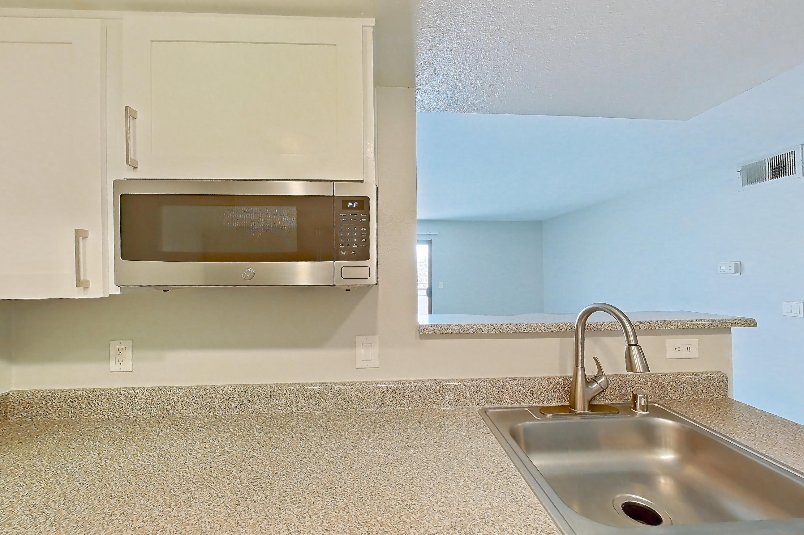 Kitchen with dishwasher, electric range, light countertops, light stone countertops, microwave, oven/range, refrigerator, stainless steel appliances, and white appliances, Apartment 08 at Avana Rancho Cucamonga