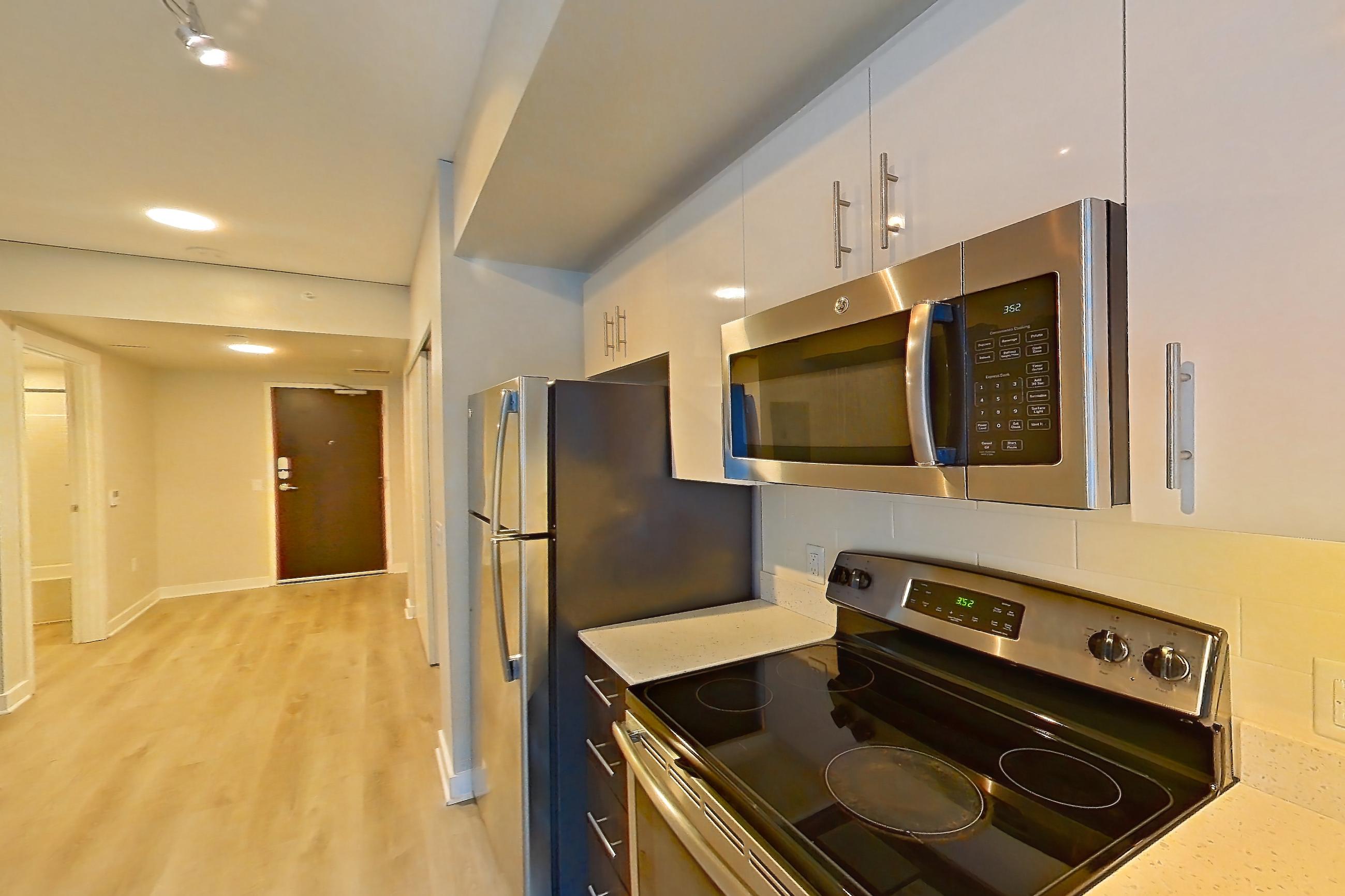 Kitchen with dishwasher, electric range, light countertops, light stone countertops, light wood-finish flooring, oven/range, refrigerator, and stainless steel appliances, Apartment 0-0805 at Cielo