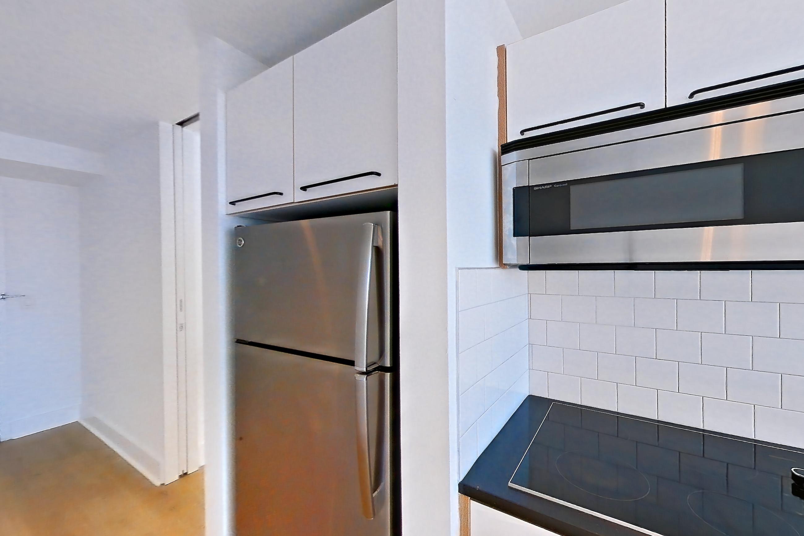 Kitchen with black appliances, cooktop, dark countertops, electric cooktop, light countertops, light wood-finish flooring, microwave, oven/range, refrigerator, and stainless steel appliances, Apartment SAB-3205 at Sable