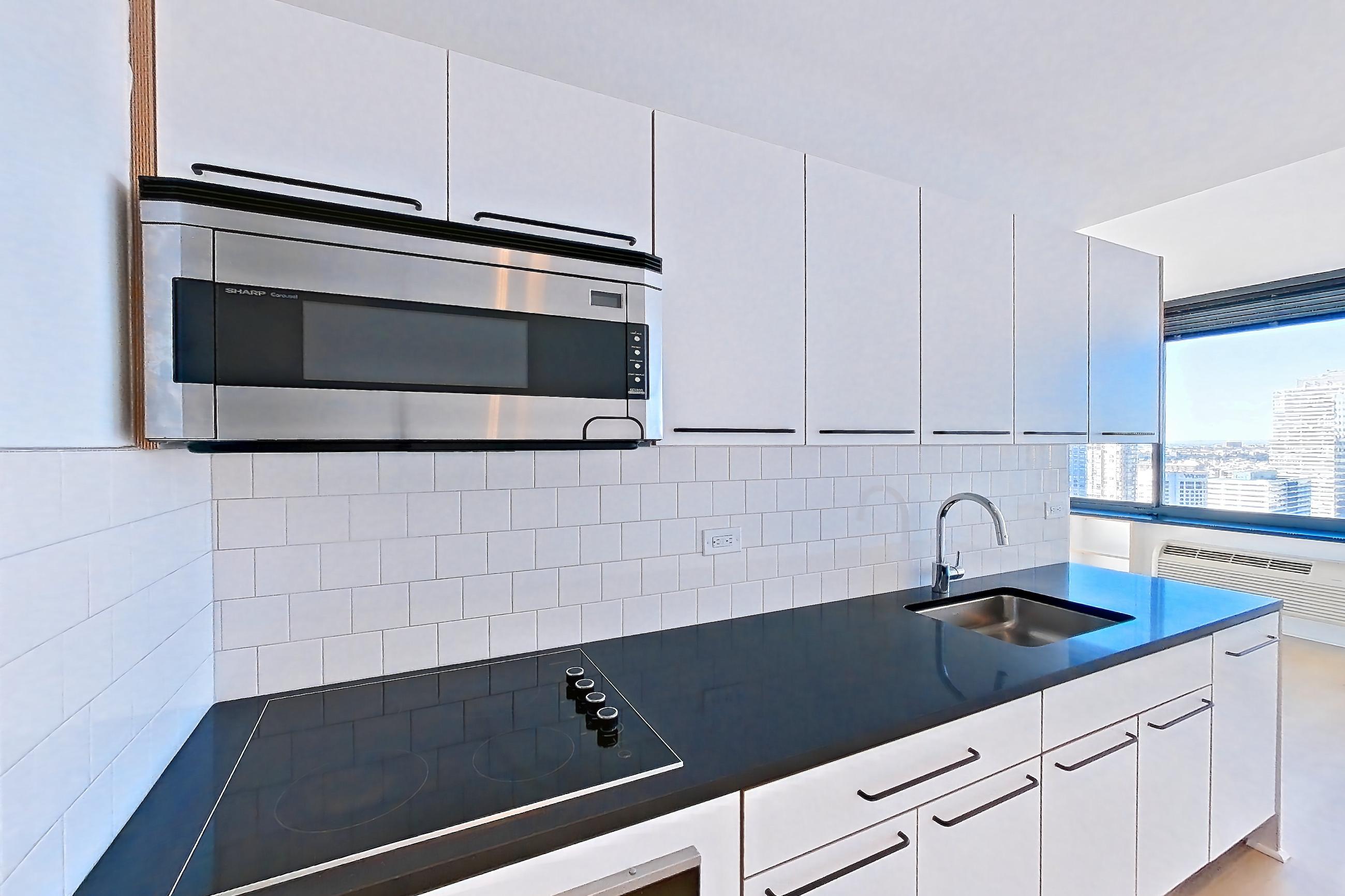 Kitchen with black appliances, cooktop, dark countertops, electric cooktop, light countertops, light wood-finish flooring, microwave, oven/range, refrigerator, and stainless steel appliances, Apartment SAB-3205 at Sable