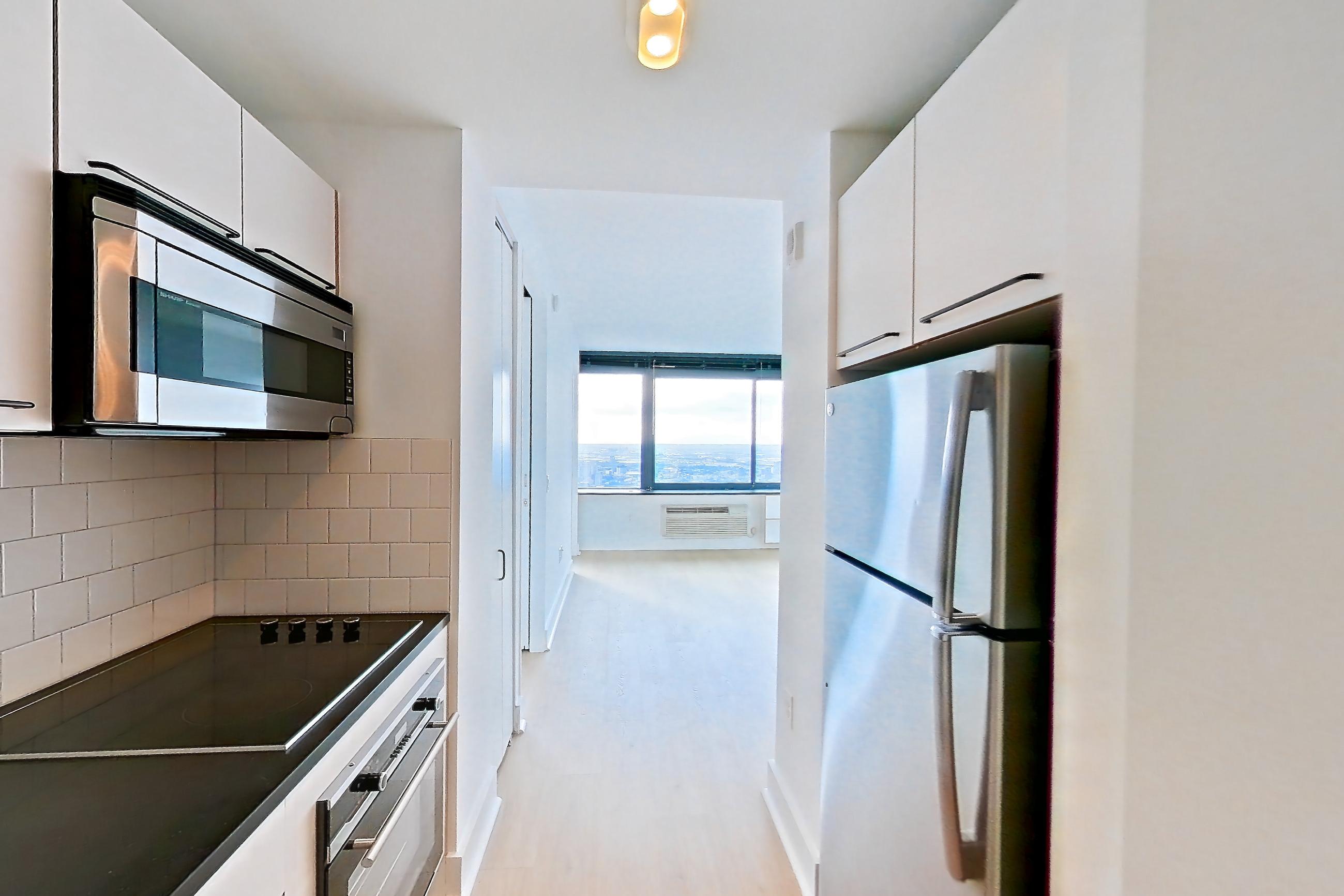 Kitchen with black appliances, cooktop, dark countertops, electric cooktop, light countertops, light wood-finish flooring, refrigerator, and stainless steel appliances, Apartment SAB-6906 at Sable