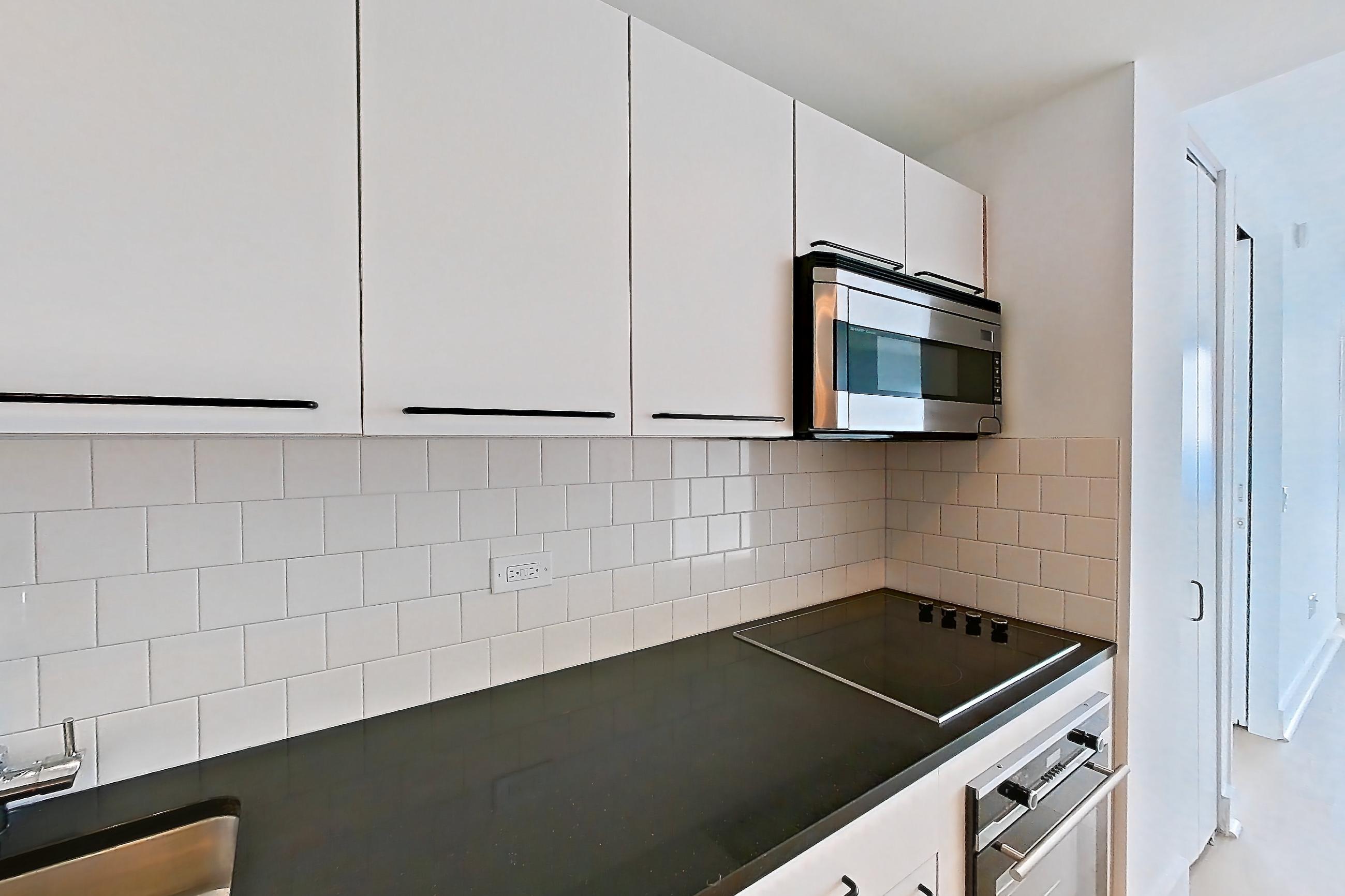 Kitchen with black appliances, cooktop, dark countertops, electric cooktop, light countertops, light wood-finish flooring, refrigerator, and stainless steel appliances, Apartment SAB-6906 at Sable
