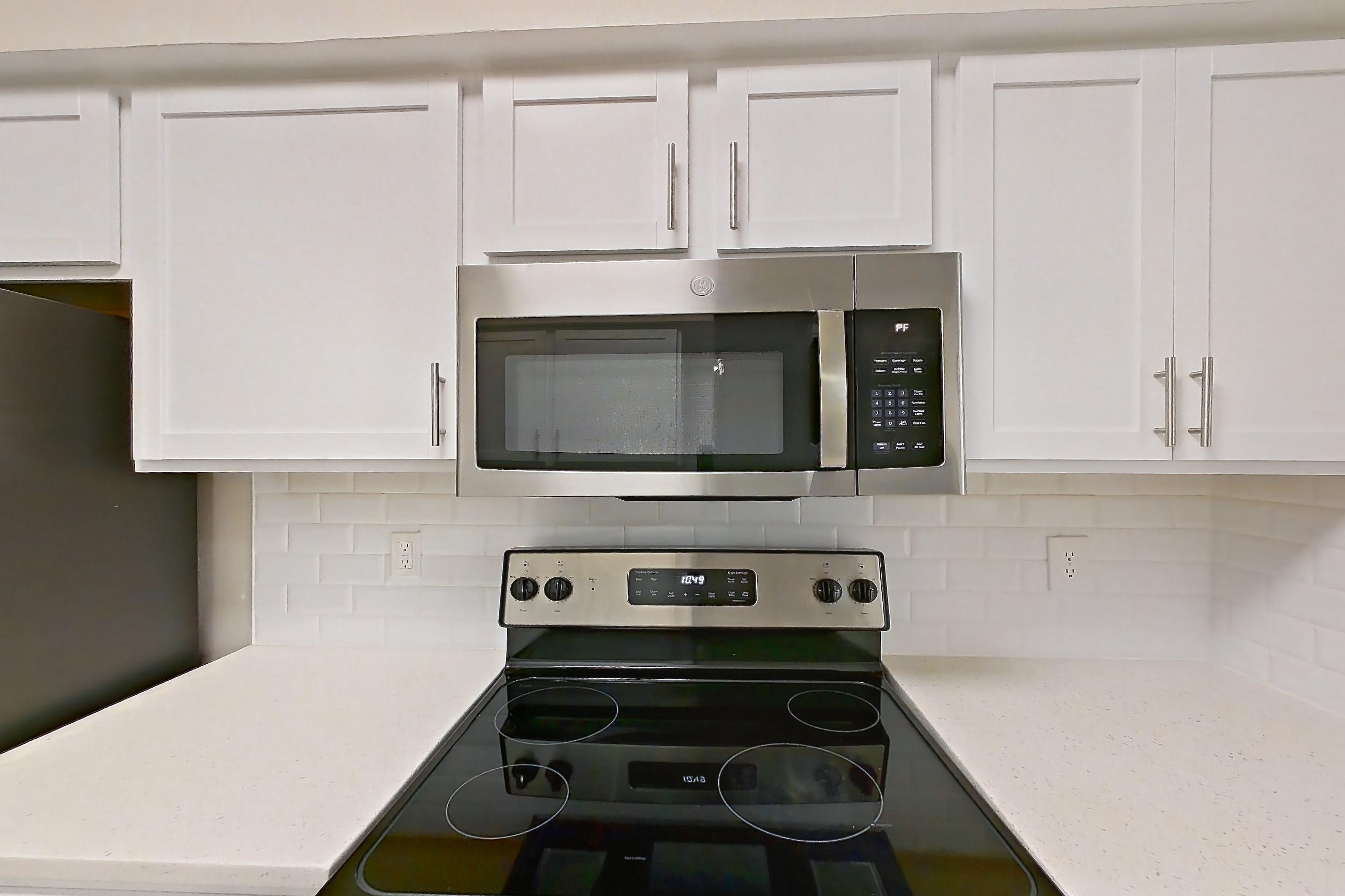 Kitchen with dishwasher, electric range, light countertops, light stone countertops, light wood-finish flooring, oven/range, refrigerator, and stainless steel appliances, Apartment 4314 at Marq Perimeter