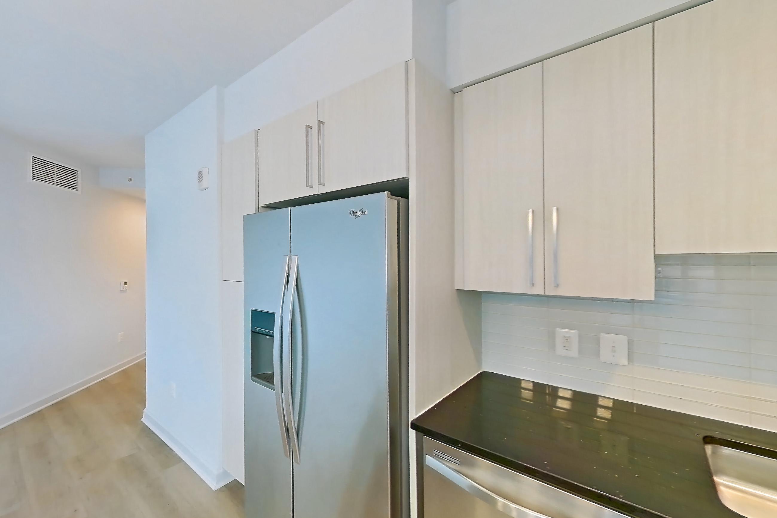 Kitchen with dark stone countertops, dishwasher, double oven, electric range, light countertops, light wood-finish flooring, microwave, oven/range, refrigerator, and stainless steel appliances, Apartment 0404 at Latitude