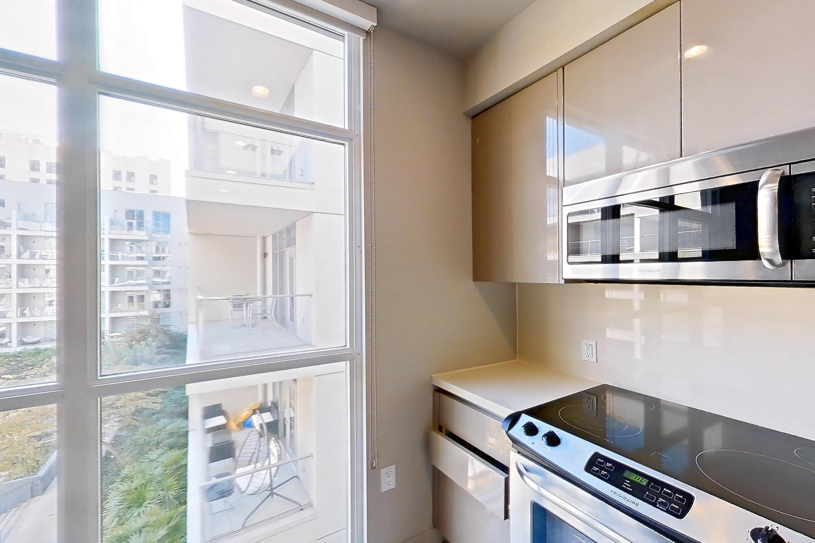 Kitchen with electric range, light countertops, light stone countertops, light wood-finish flooring, oven/range, refrigerator, and stainless steel appliances, Apartment 0-5006 at Eighth and Grand