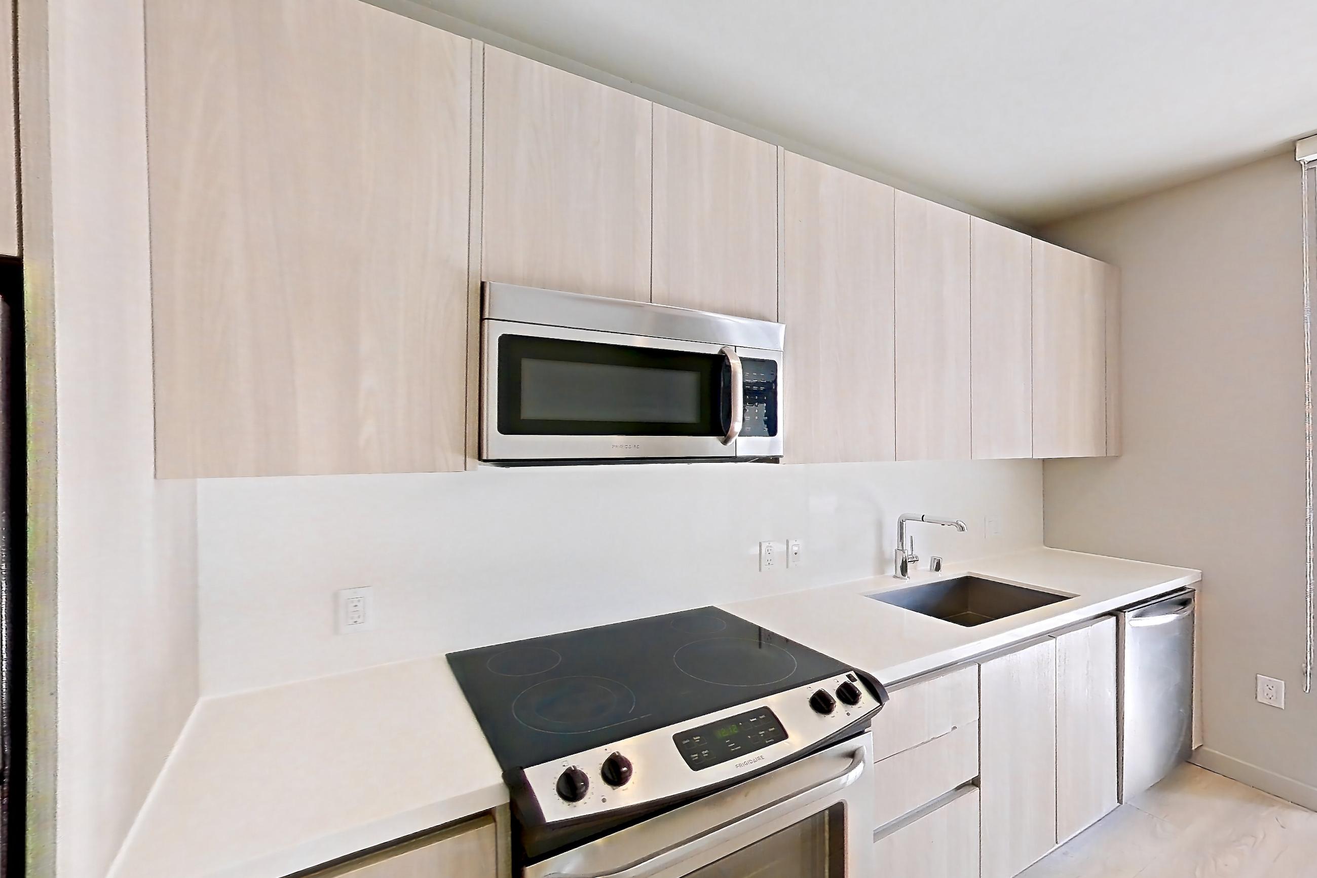 Kitchen with electric range, light countertops, light wood-finish flooring, microwave, oven/range, refrigerator, and stainless steel appliances, Apartment 0-5125 at Eighth and Grand