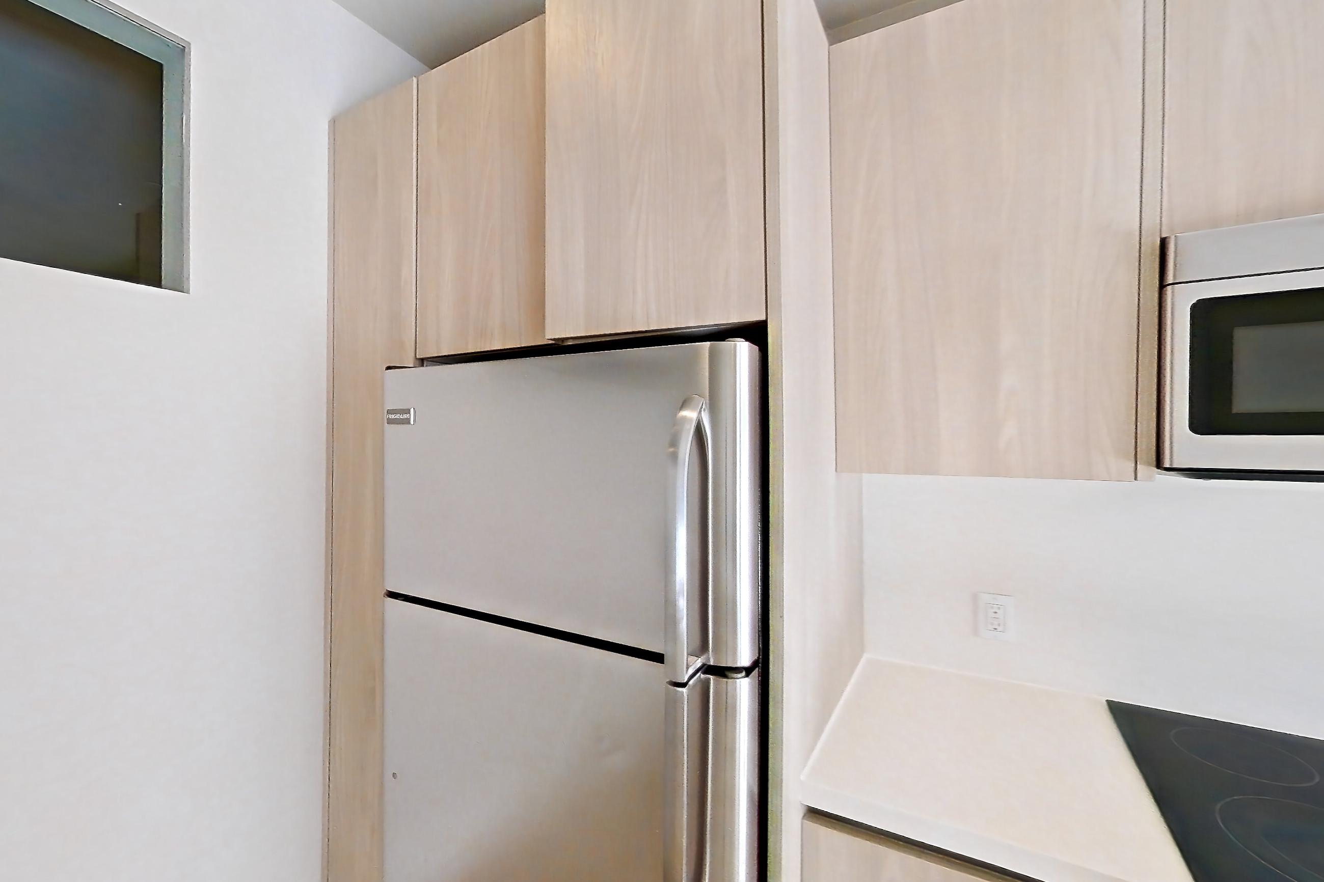 Kitchen with electric range, light countertops, light wood-finish flooring, microwave, oven/range, refrigerator, and stainless steel appliances, Apartment 0-5125 at Eighth and Grand