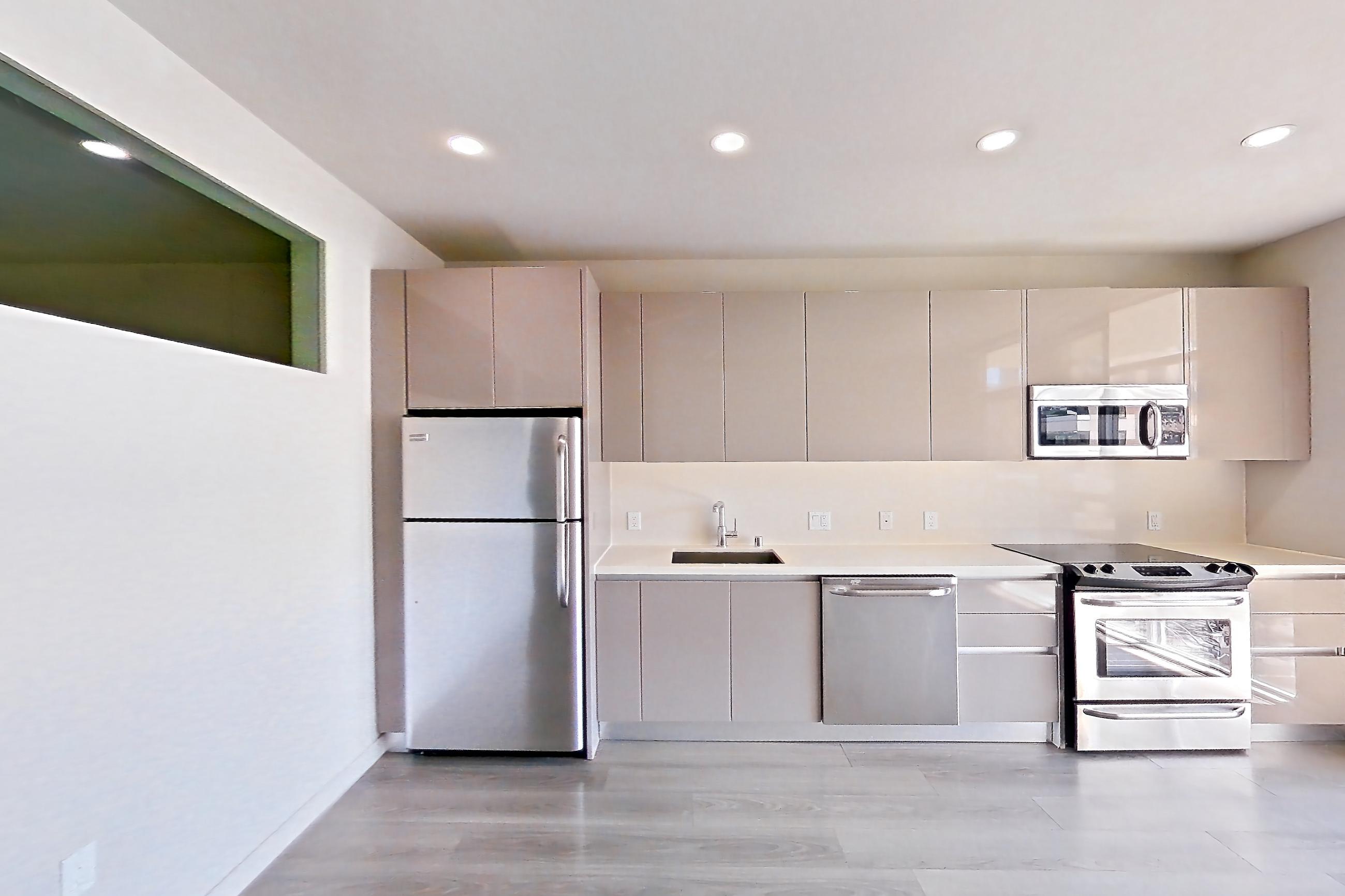 Living room with light countertops, light wood-finish flooring, refrigerator, and stainless steel appliances, Apartment 0-5169 at Eighth and Grand