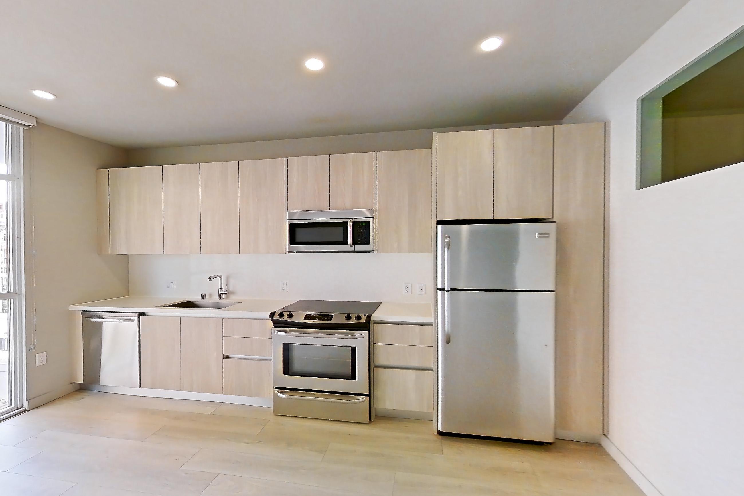 Living room with electric range, light countertops, light wood-finish flooring, microwave, oven/range, refrigerator, and stainless steel appliances, Apartment 0-6137 at Eighth and Grand