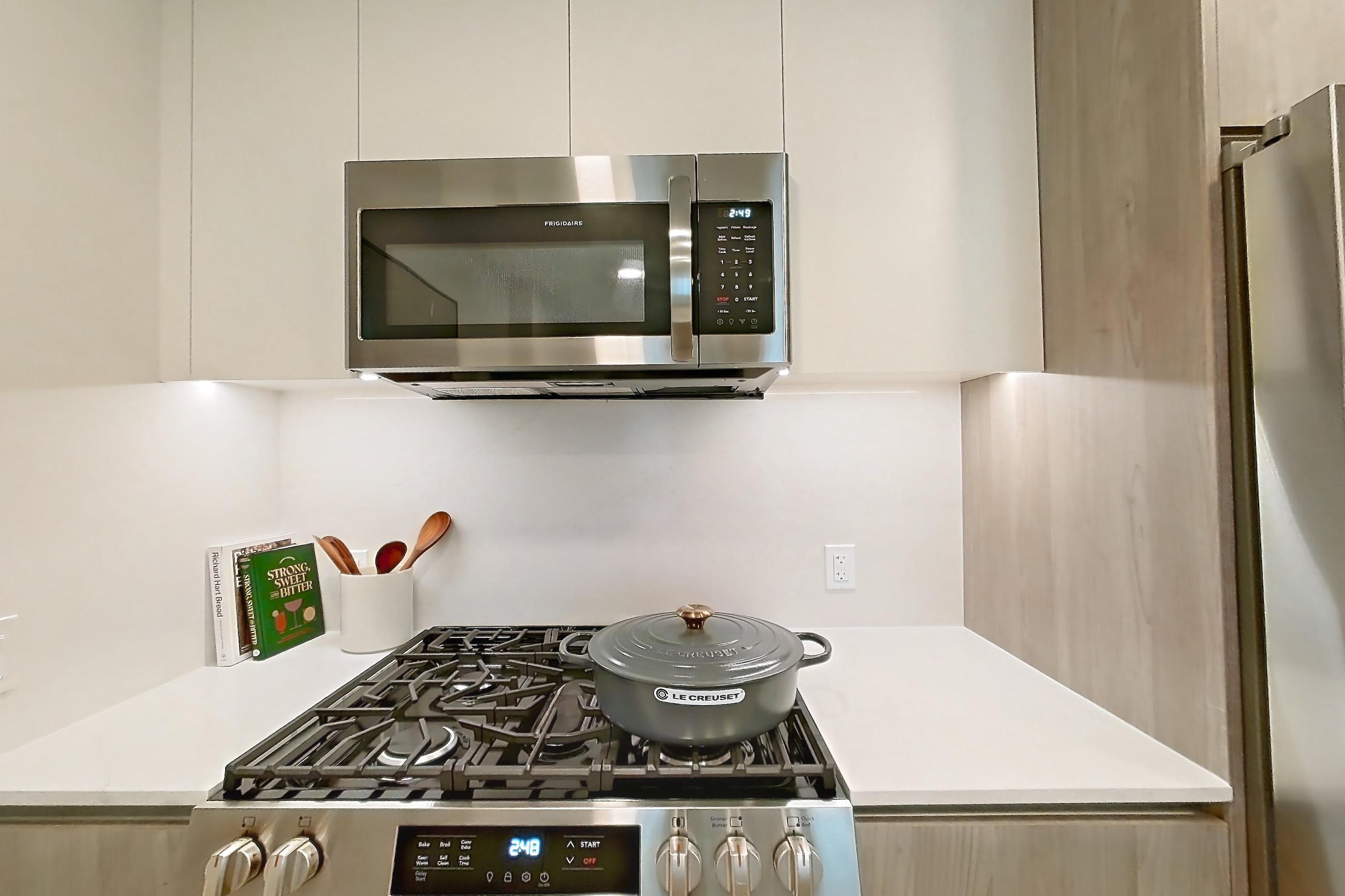 Kitchen with gas range, light countertops, light stone countertops, light wood-finish flooring, microwave, oven/range, refrigerator, and stainless steel appliances, Apartment 909 at Loden