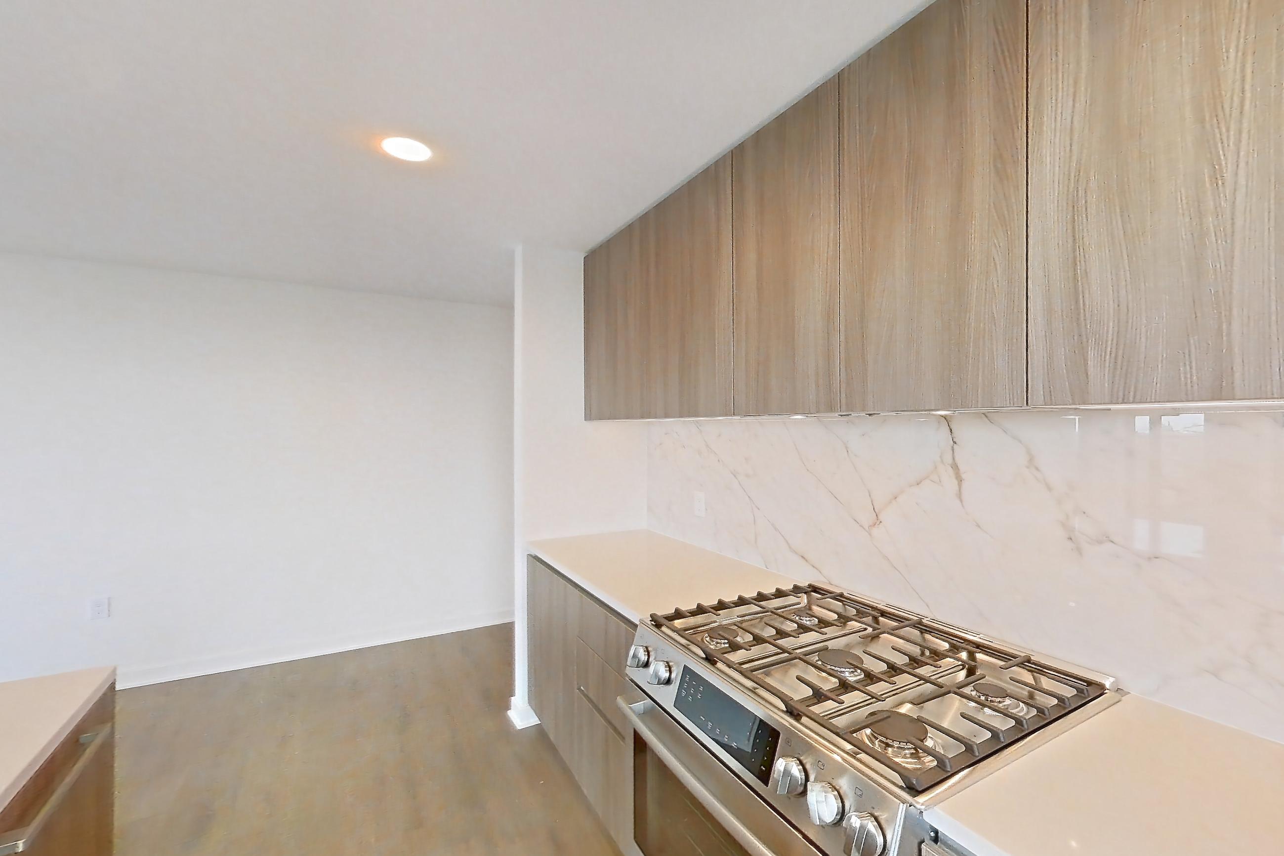 Kitchen with black appliances, cooktop, electric cooktop, gas range, light stone countertops, light tile flooring, light wood-finish flooring, oven/range, and stainless steel appliances, Apartment 0622 at Aerie