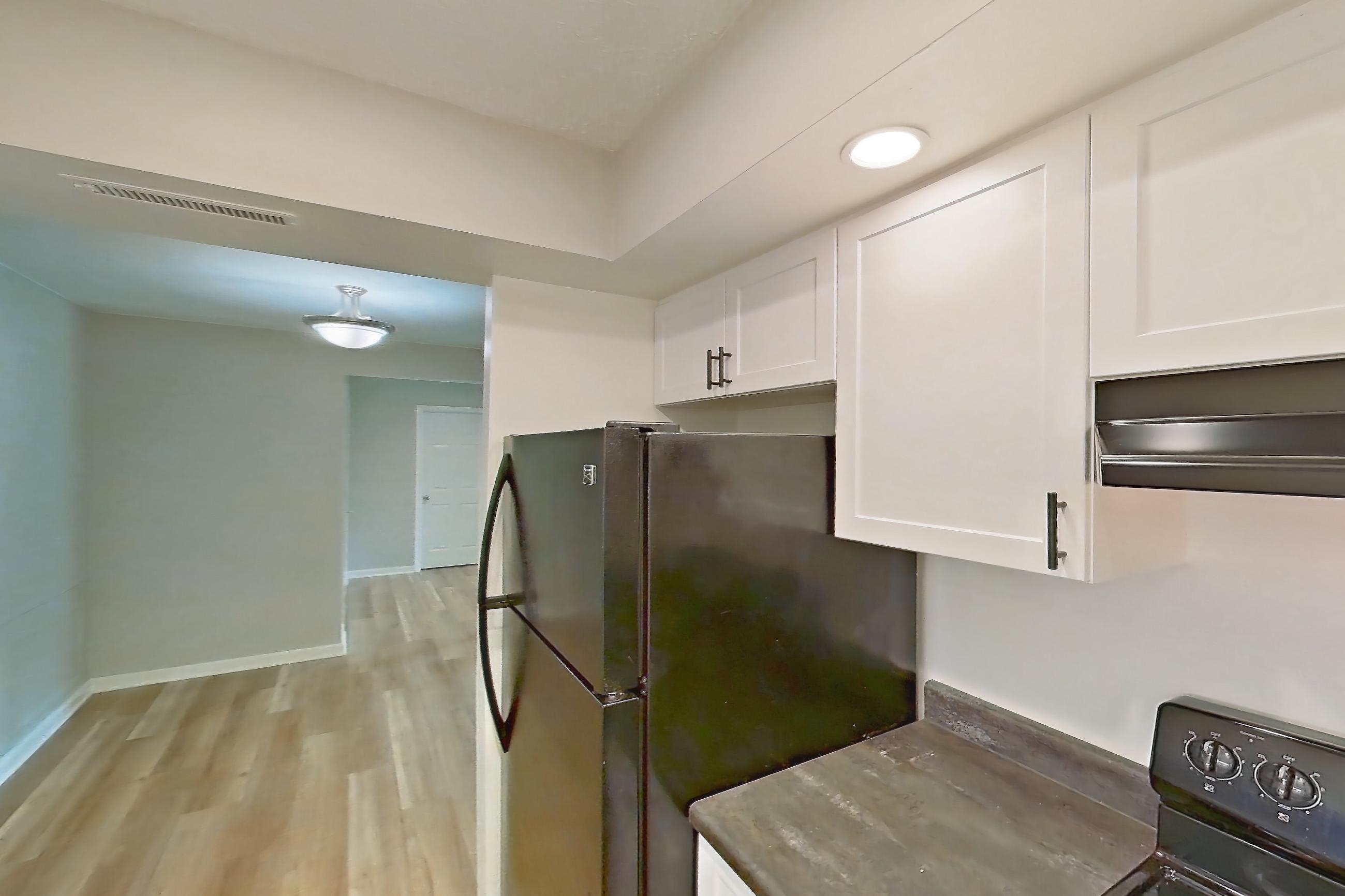 Kitchen with black appliances, dark stone countertops, electric range, light wood-finish flooring, oven/range, refrigerator, and stainless steel appliances, Apartment 5148-3TR at Canterbury Green