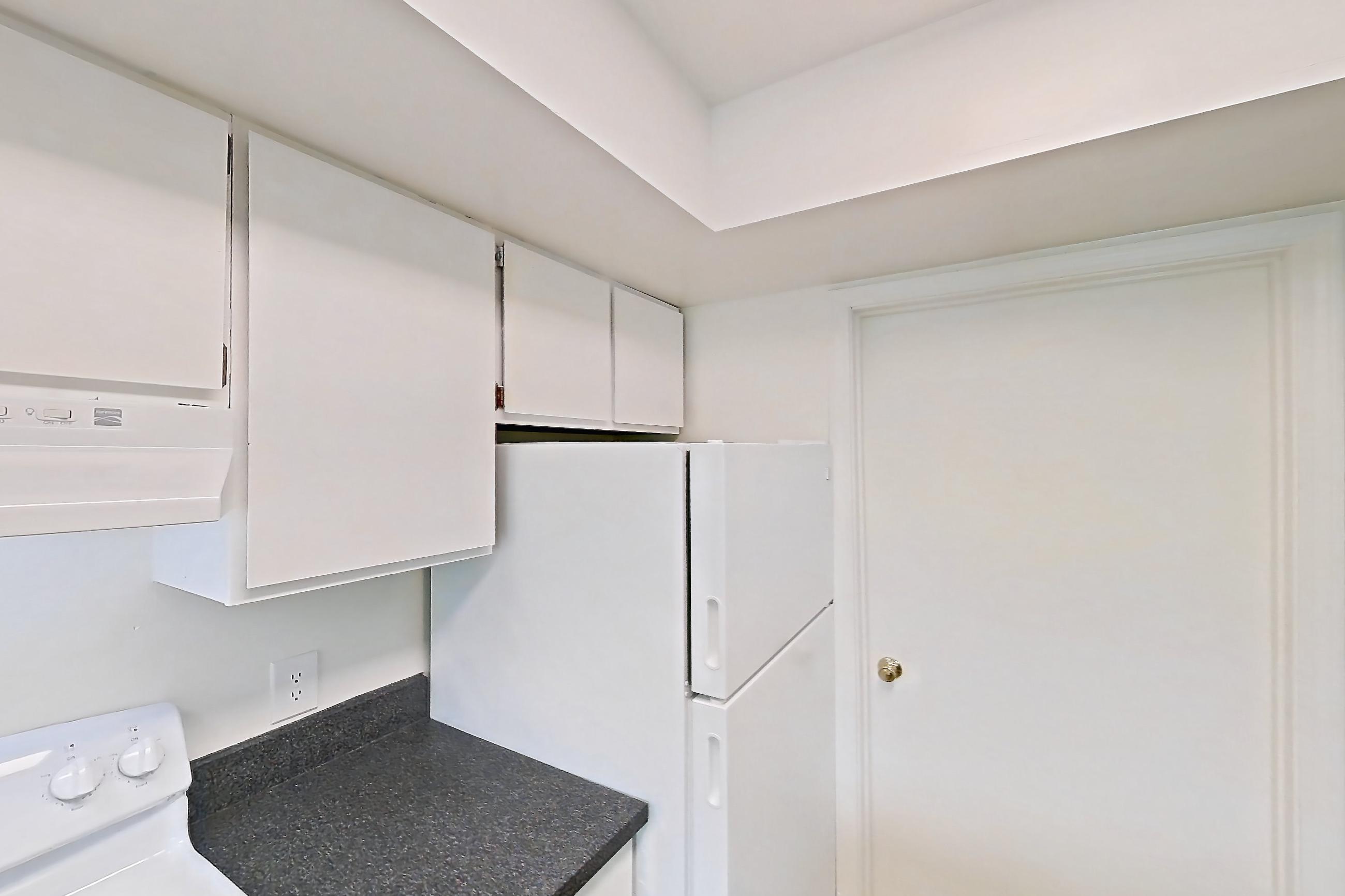 Kitchen with black appliances, dark countertops, dark stone countertops, dishwasher, electric range, light wood-finish flooring, oven/range, refrigerator, and white appliances, Apartment 5242ST at Canterbury Green