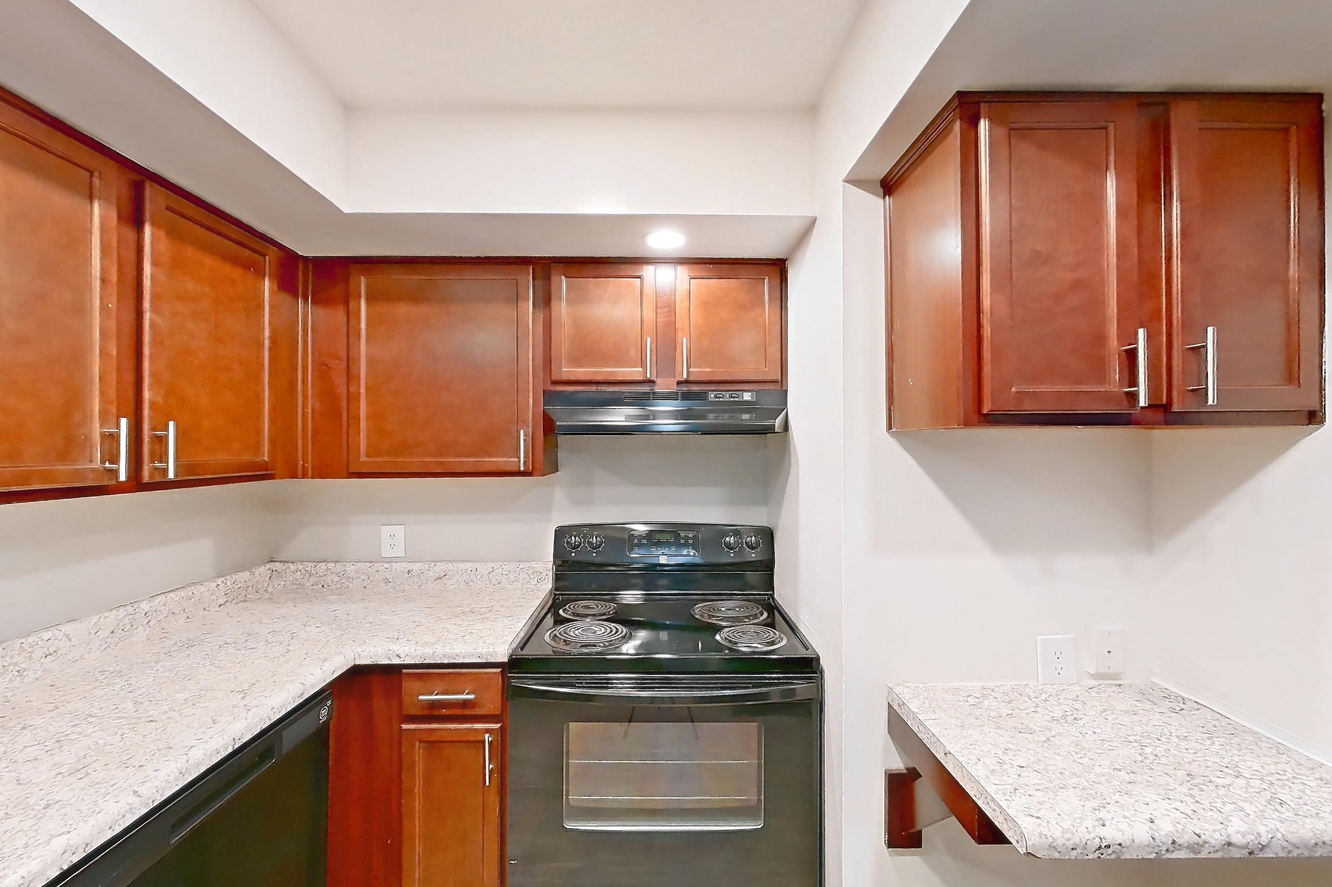 Kitchen with black appliances, dishwasher, light stone countertops, light wood-finish flooring, oven/range, range hood, and refrigerator, Apartment 3018-4CA at Canterbury Green