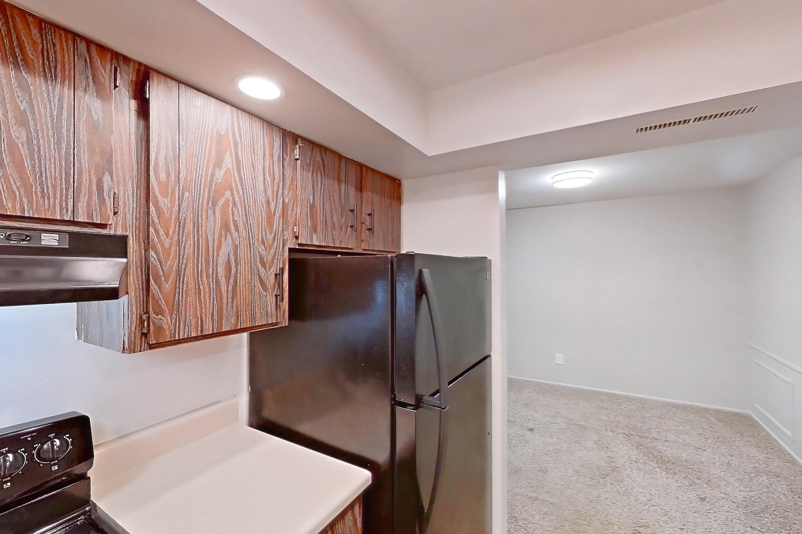 Kitchen with black appliances, electric range, light carpet, light countertops, light wood-finish flooring, oven/range, refrigerator, stainless steel appliances, and wood-finish flooring, Apartment 2421-6AB at Canterbury Green