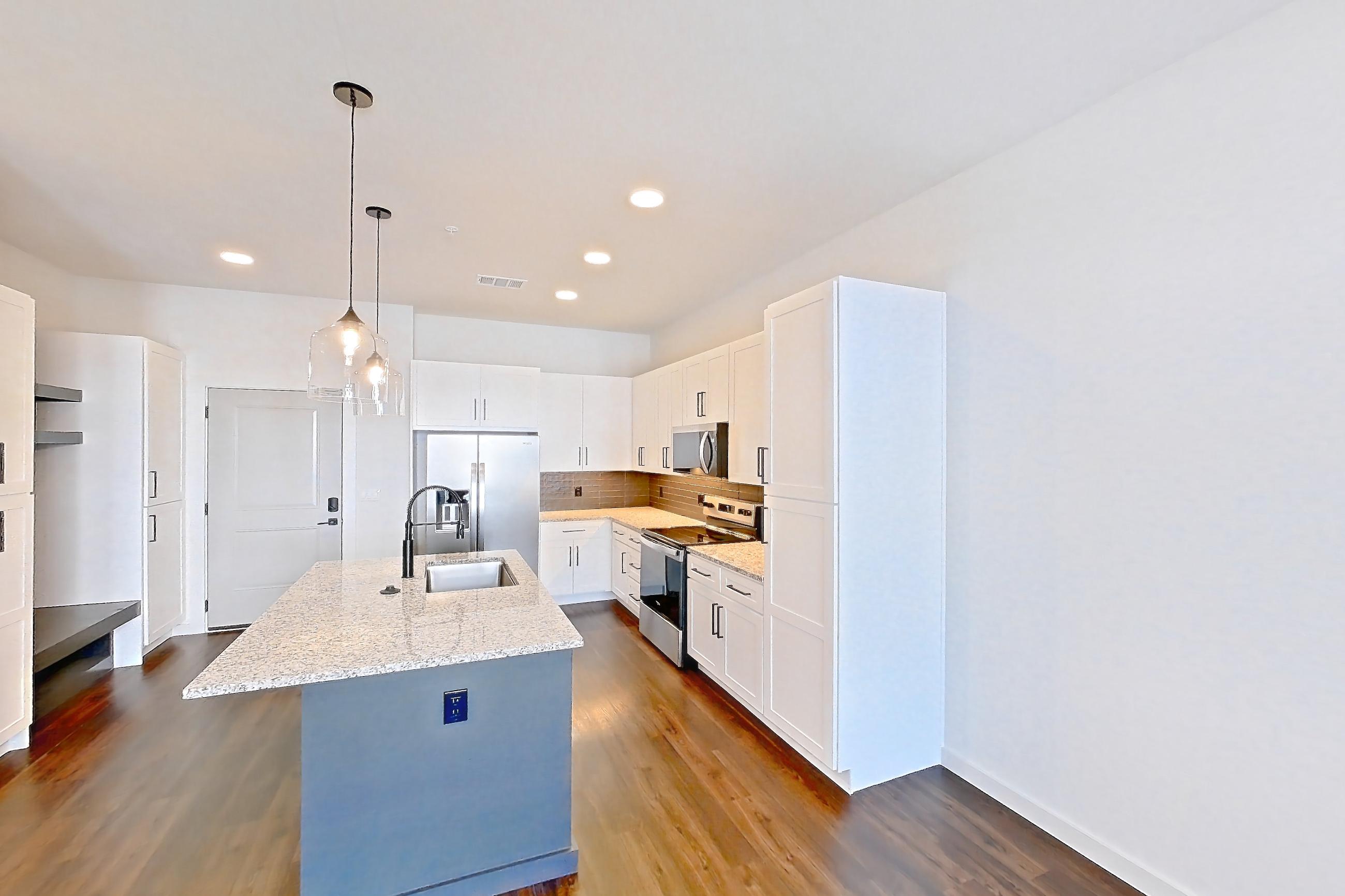 Living space with dark wood-finish flooring, electric range, kitchen island, light countertops, light stone countertops, oven/range, refrigerator, stainless steel appliances, and water & ice dispenser, Apartment 1-214 at Cortland Peterson