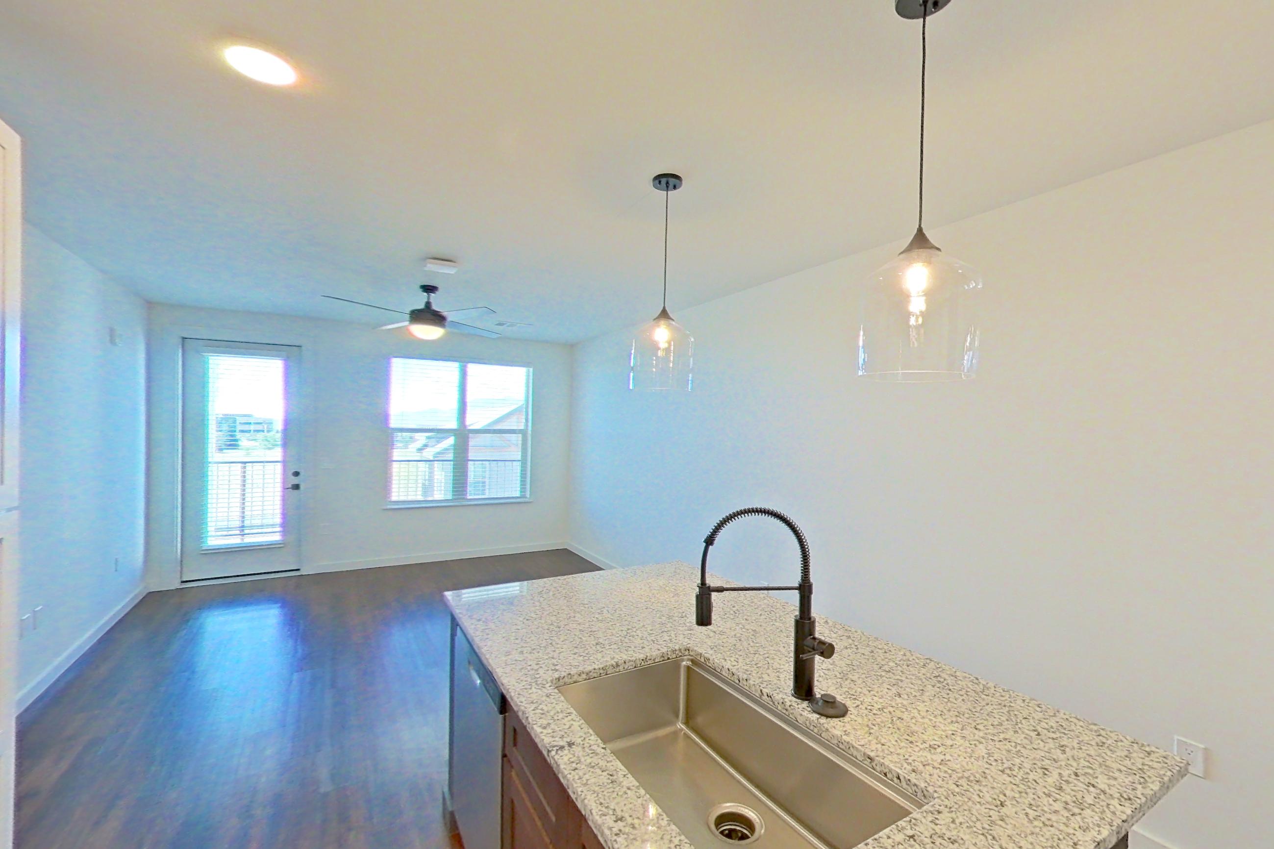 Kitchen with dark wood-finish flooring, dishwasher, electric range, kitchen island, light countertops, light stone countertops, microwave, oven/range, refrigerator, stainless steel appliances, and water & ice dispenser, Apartment 3-302 at Cortland Peterson
