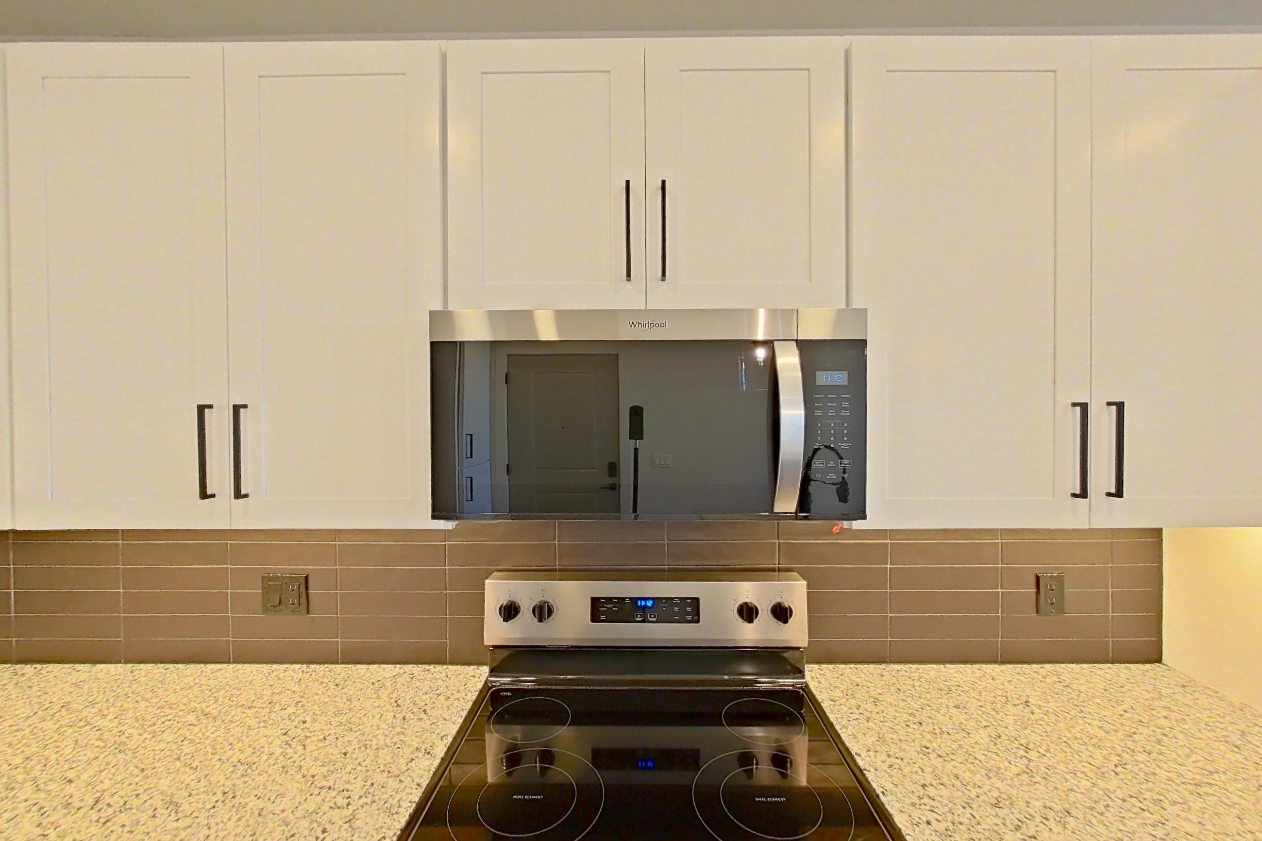 Kitchen with dark wood-finish flooring, dishwasher, electric range, kitchen island, light countertops, light stone countertops, microwave, oven/range, refrigerator, stainless steel appliances, and water & ice dispenser, Apartment 3-302 at Cortland Peterson
