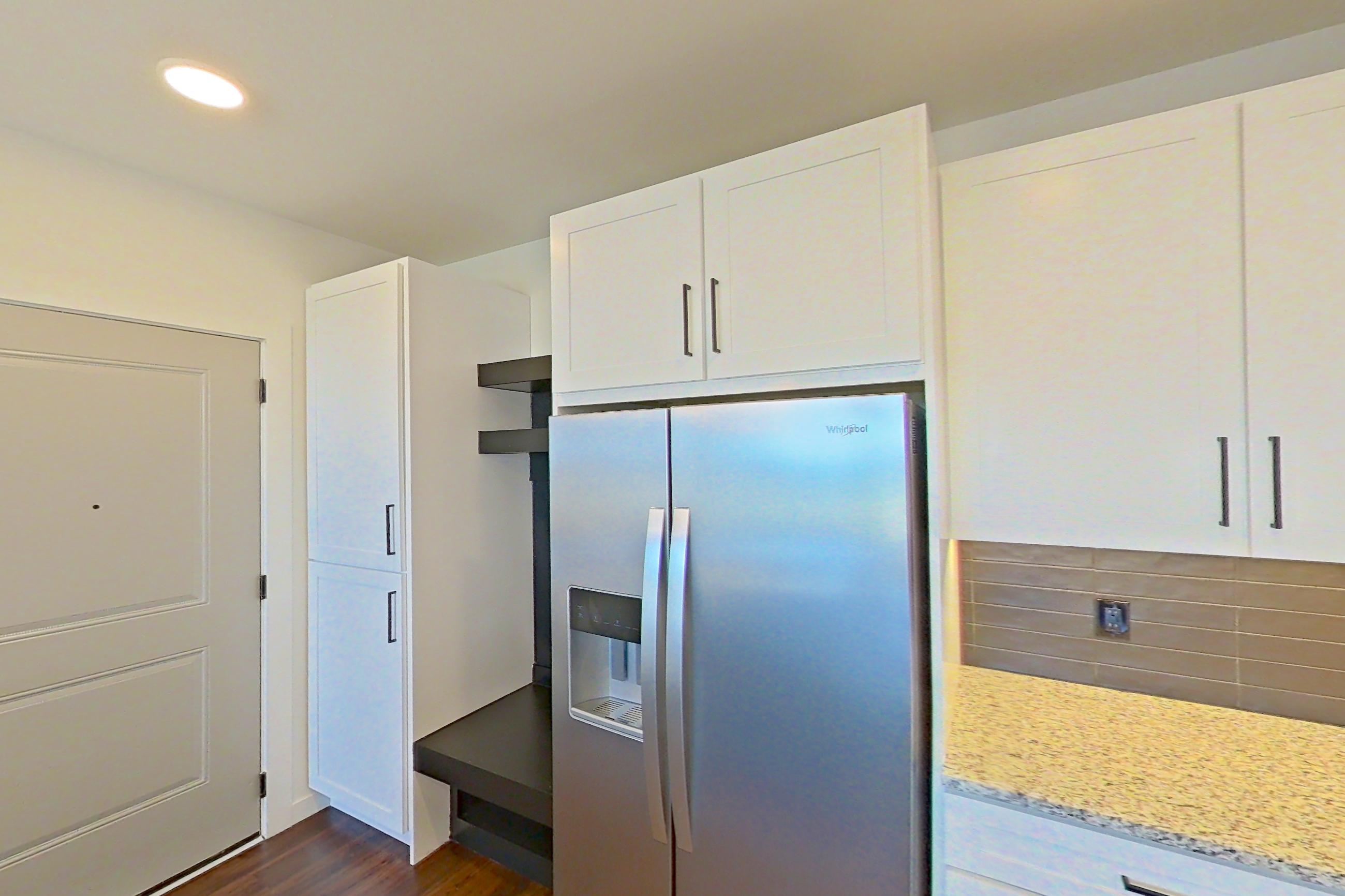 Kitchen with dark wood-finish flooring, dishwasher, electric range, kitchen island, light countertops, light stone countertops, microwave, oven/range, refrigerator, stainless steel appliances, and water & ice dispenser, Apartment 3-302 at Cortland Peterson