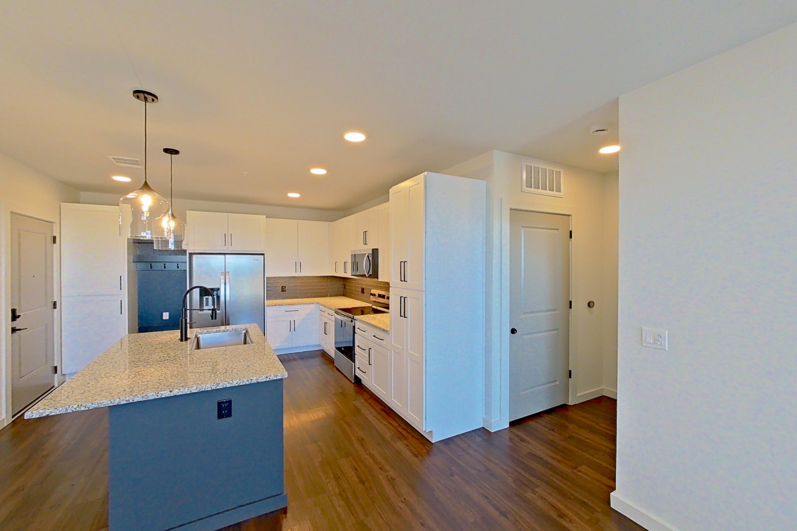 Living space with dark wood-finish flooring, electric range, kitchen island, light countertops, light stone countertops, oven/range, refrigerator, stainless steel appliances, and water & ice dispenser, Apartment 3-302 at Cortland Peterson